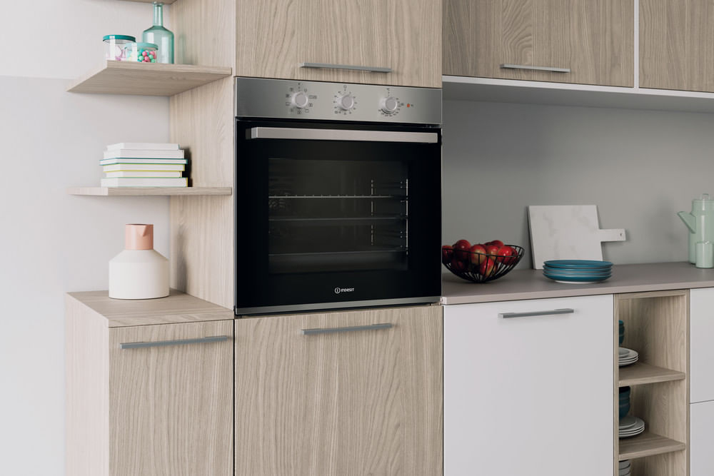 Cucina moderna con forno incassato, mobili in legno, anta bianca, mensole con libri e ciotola di frutta.