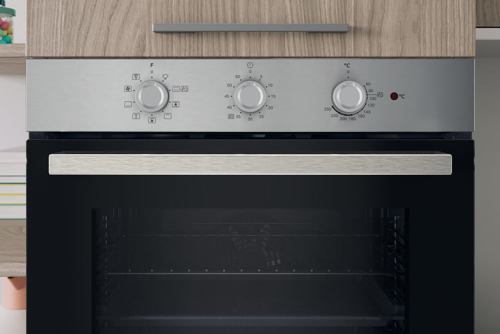 Forno da incasso argentato con tre manopole e porta in vetro nero sotto i mobili in legno.