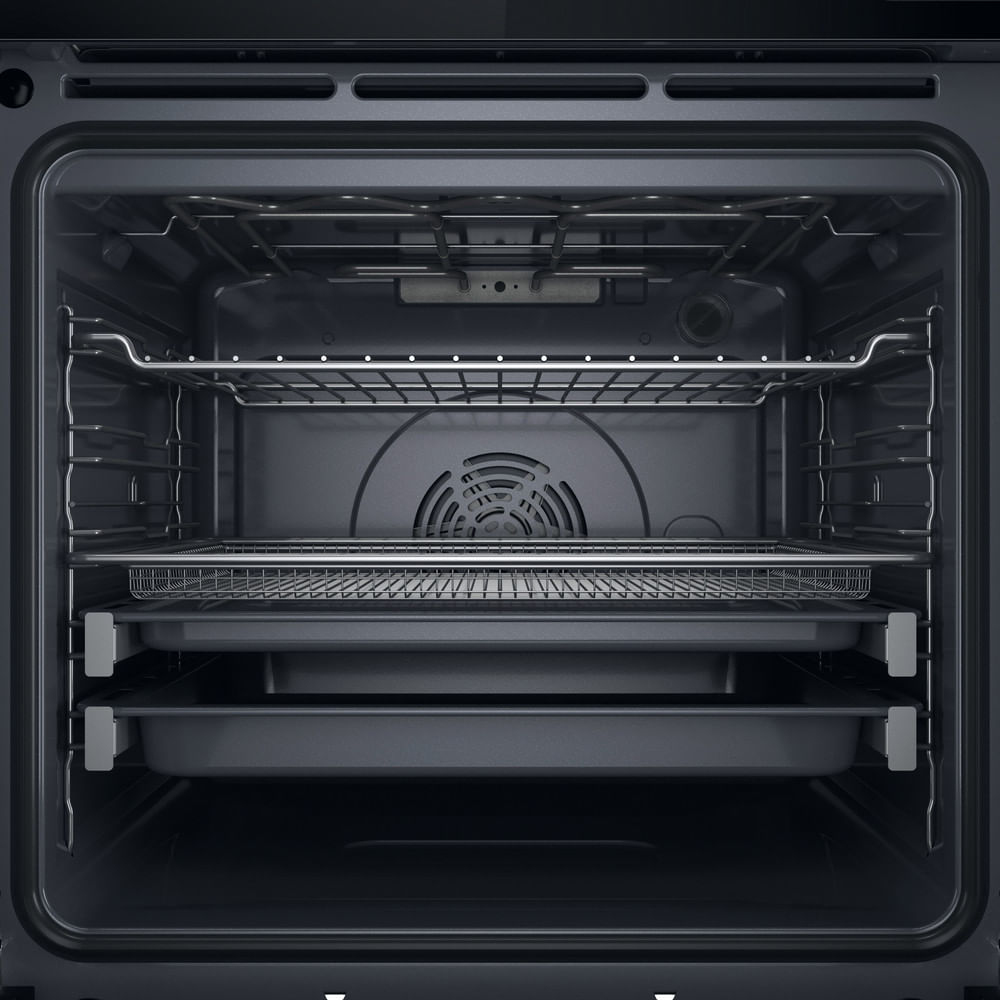 Interno nero di un forno moderno con griglie metalliche, un cestello e due teglie.