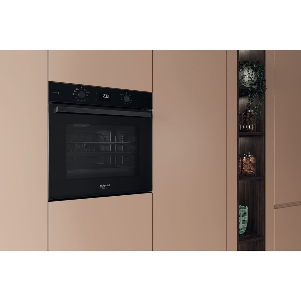 Un forno incassato nero in moderni mobili da cucina color pesca con uno scaffale scuro accanto.
