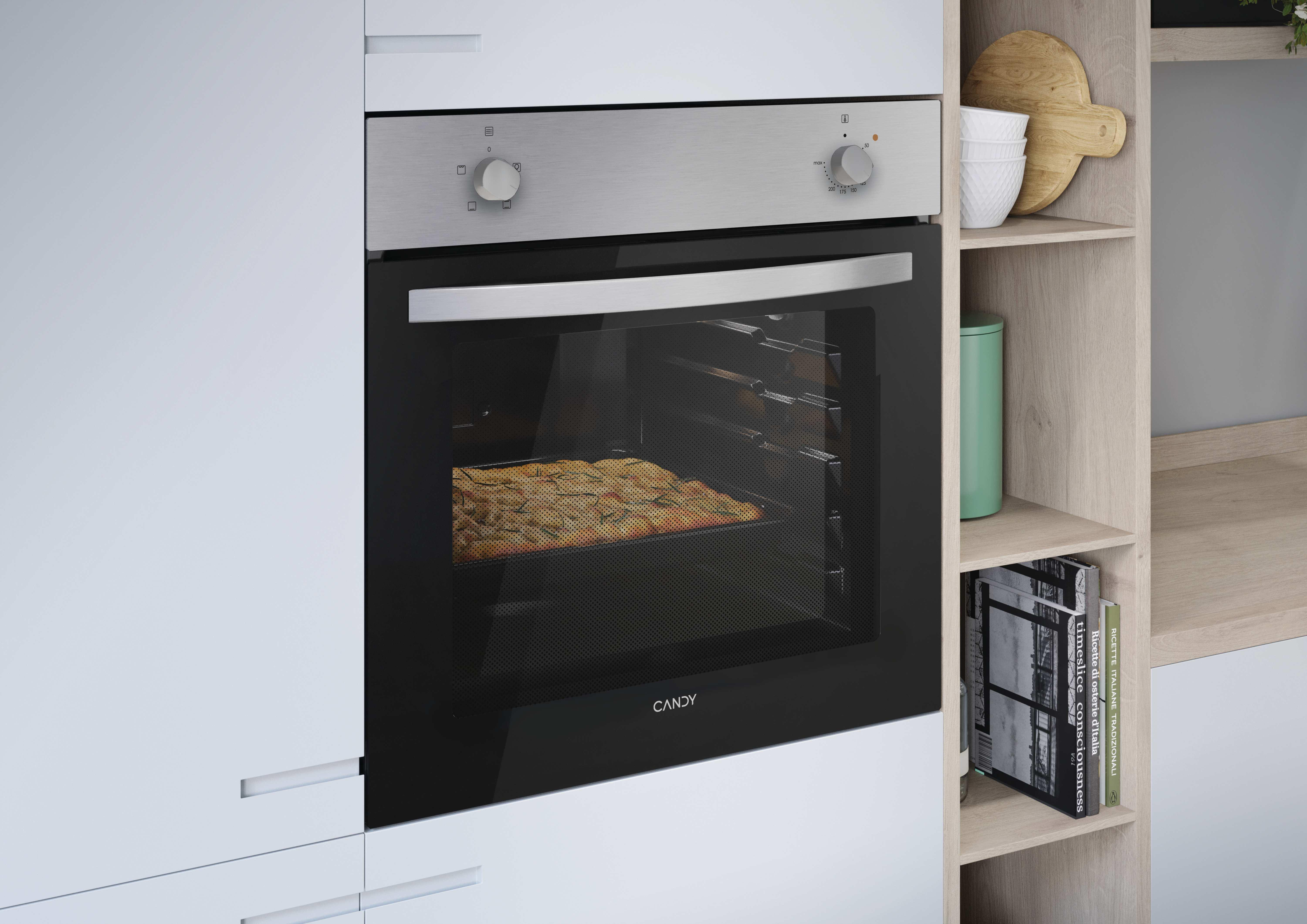Un forno da incasso Candy argentato in una cucina bianca, con cibo all'interno e mensole in legno.