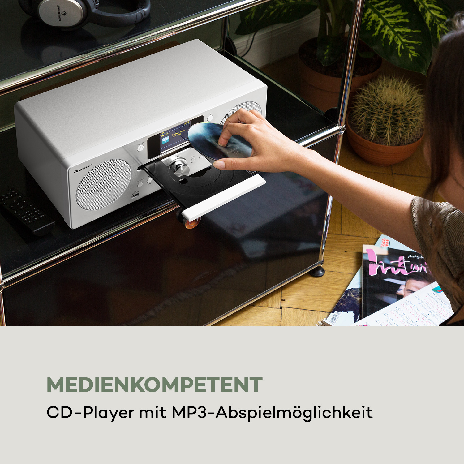 Eine Frau legt eine CD in einen silbernen auna CD-Player auf einem Glasregal ein.