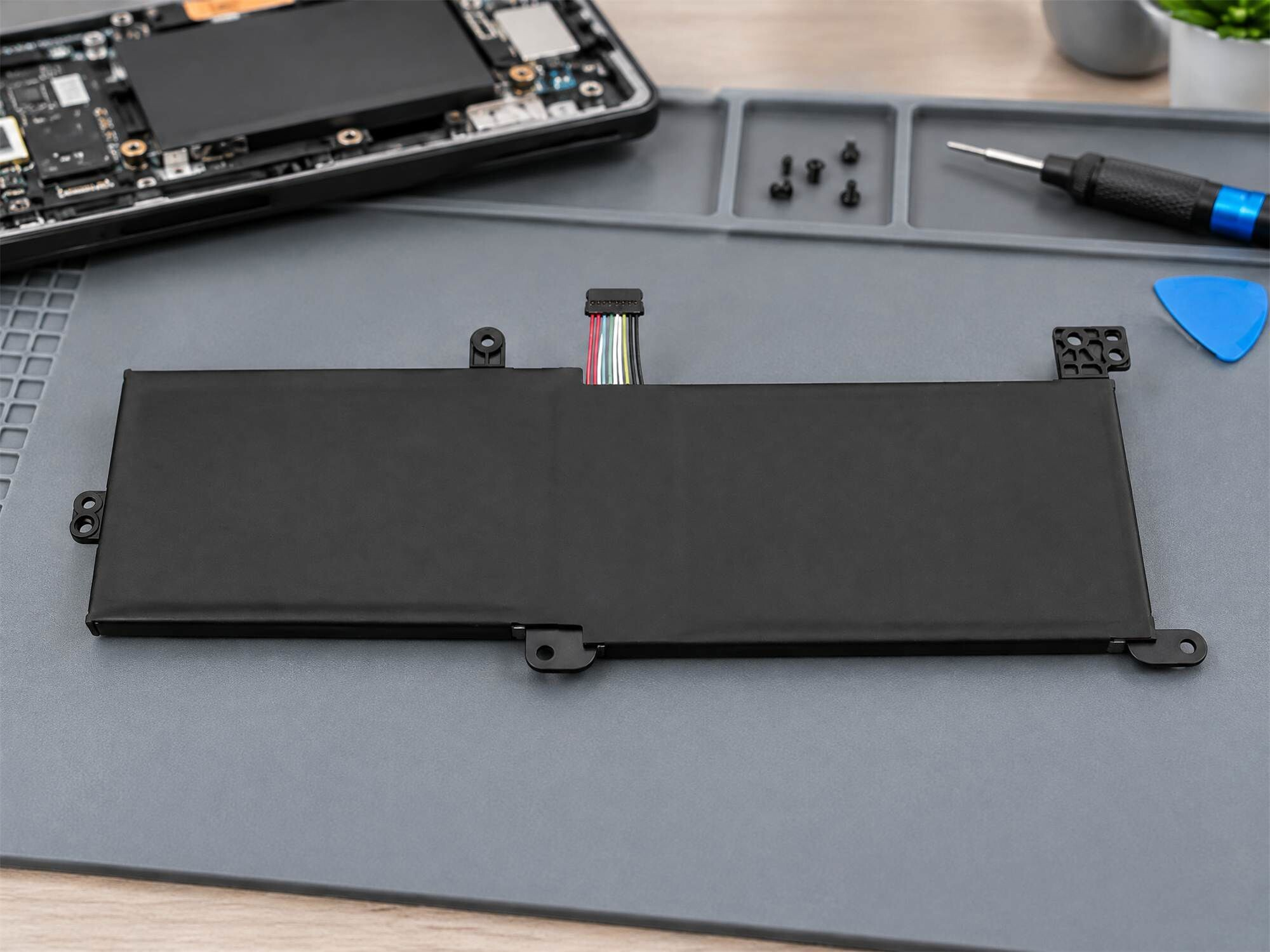 Eine schwarze Laptop-Batterie mit bunten Kabeln liegt auf einer grauen Reparaturmatte.
