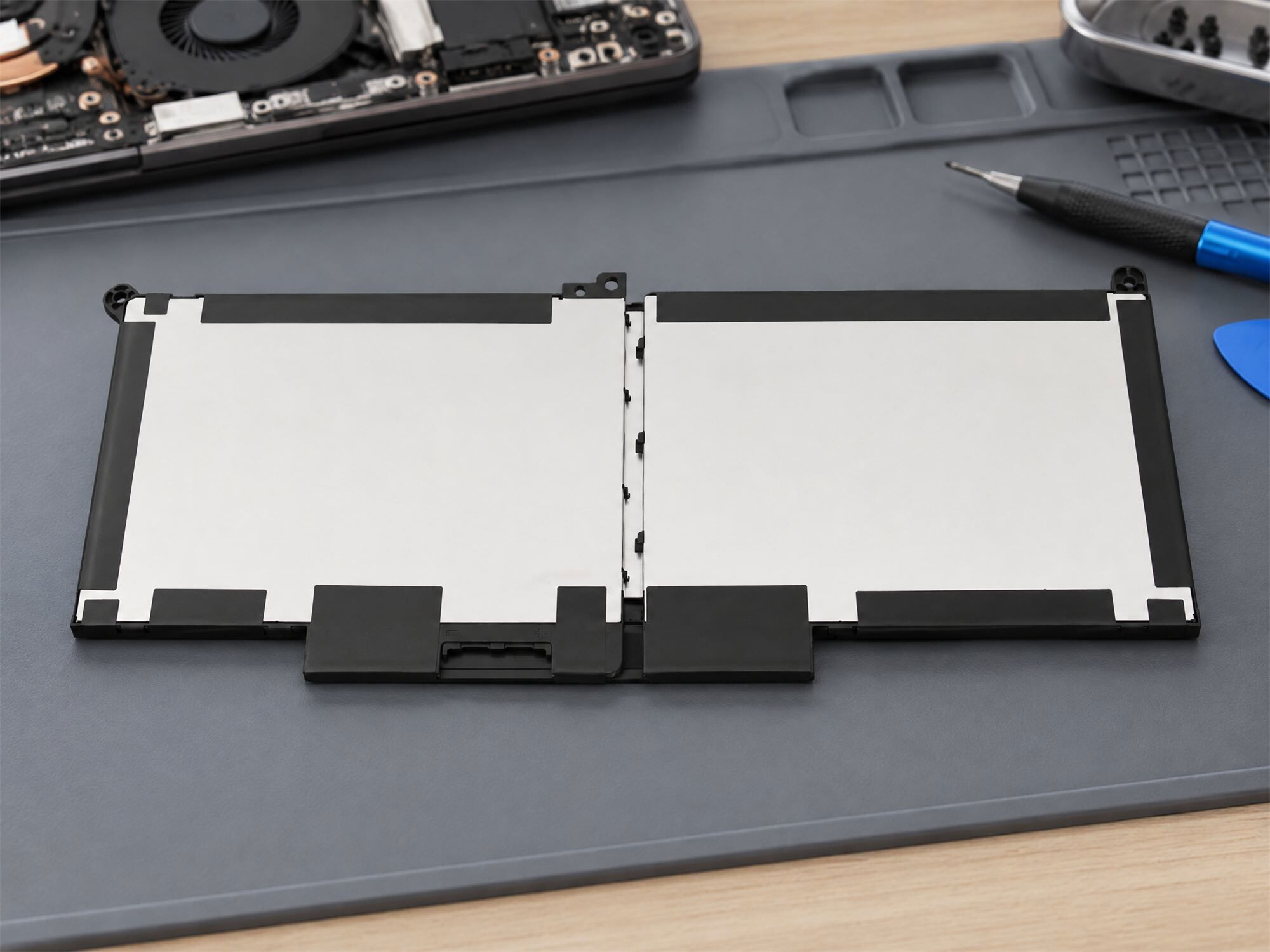 Laptop-Akku auf einer grauen Reparaturmatte mit Werkzeugen und Laptop-Teilen.