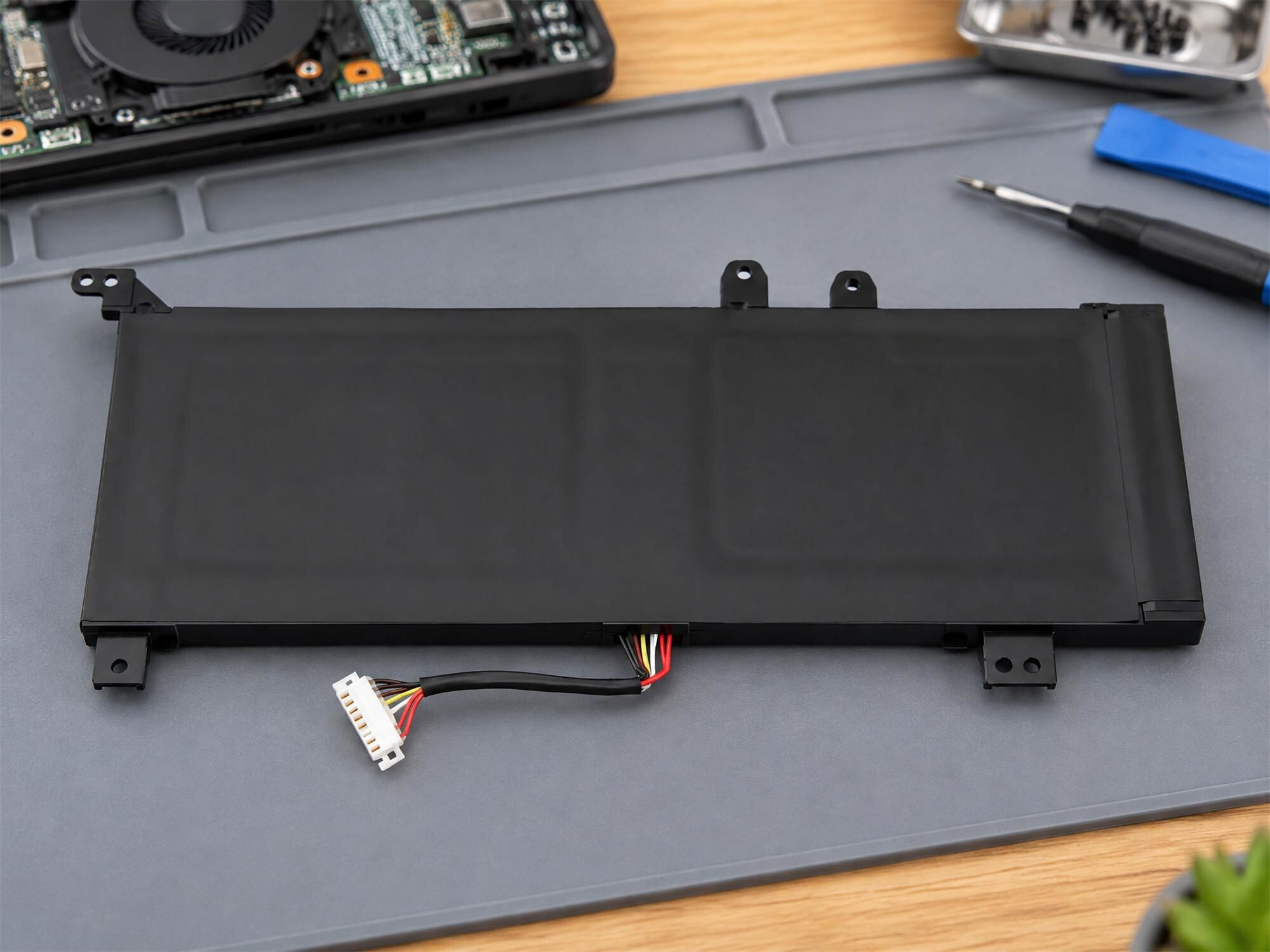 Eine schwarze Laptop-Batterie mit angeschlossenem Kabel liegt auf einer grauen Reparaturmatte.