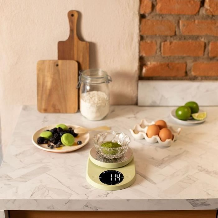 Una bilancia da cucina con una ciotola di polvere verde su un piano in marmo.