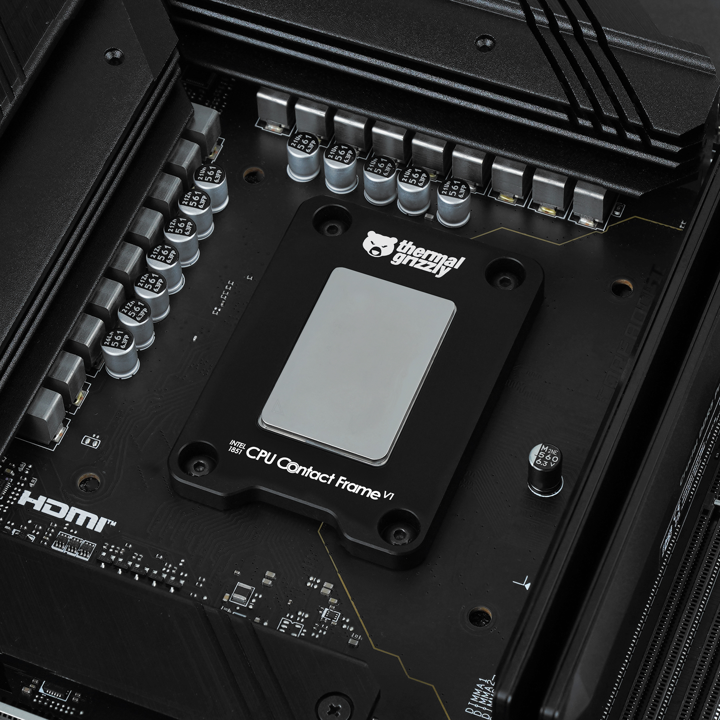 Ein schwarzer Thermal Grizzly CPU Kontaktrahmen V1 auf einem Mainboard mit Kondensatoren.