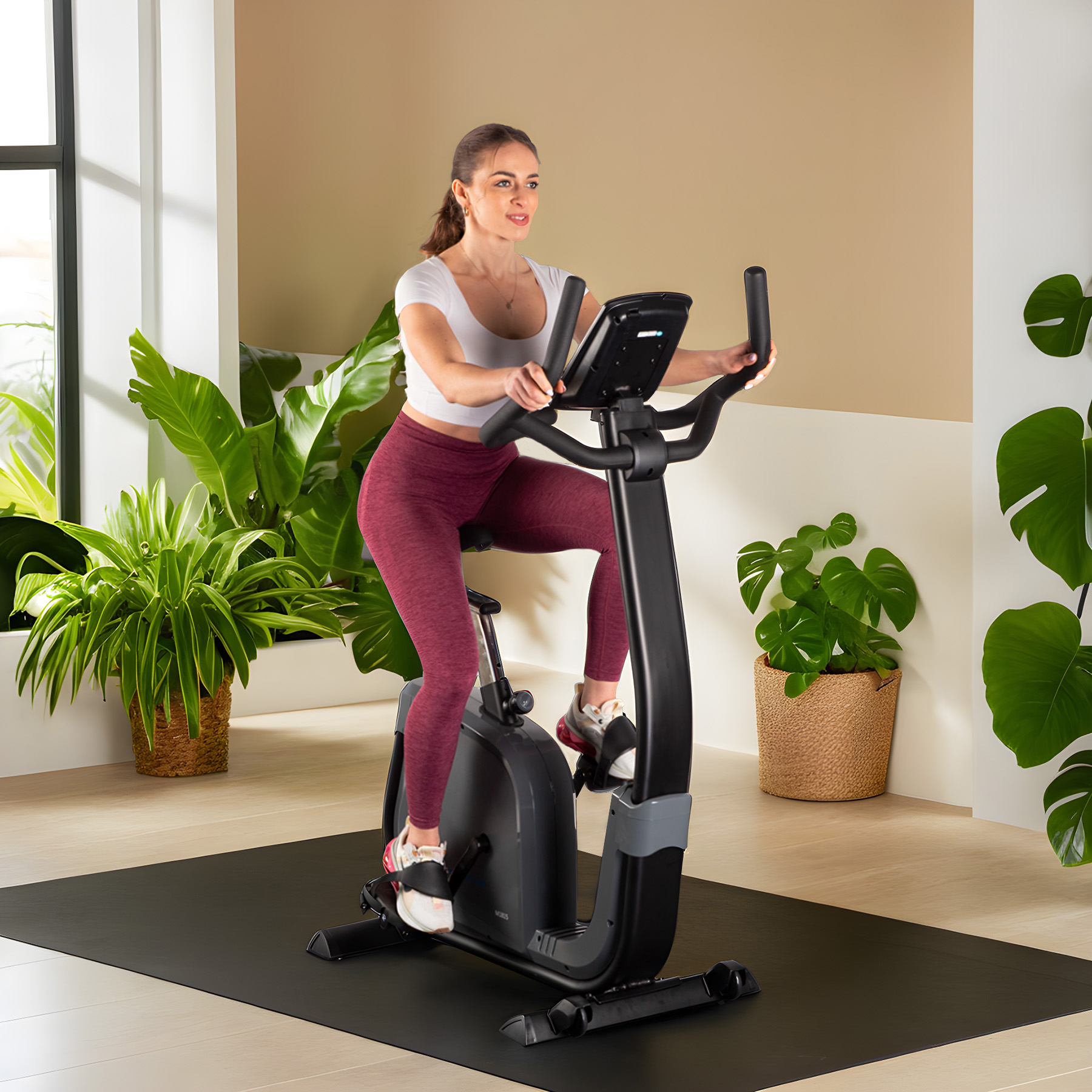 Kobieta w stroju sportowym ćwiczy na rowerku stacjonarnym w jasnym pokoju z roślinami.