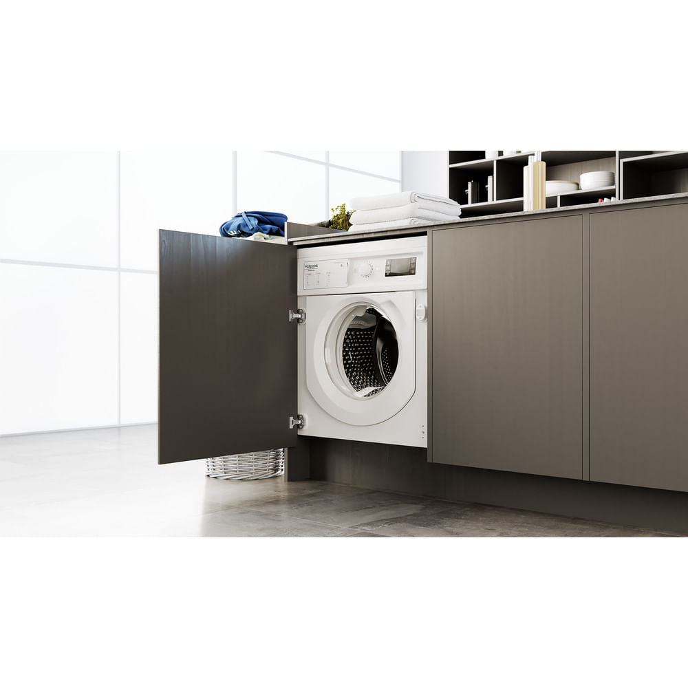 Una lavatrice da incasso bianca è installata in una cucina moderna con mobili grigi.