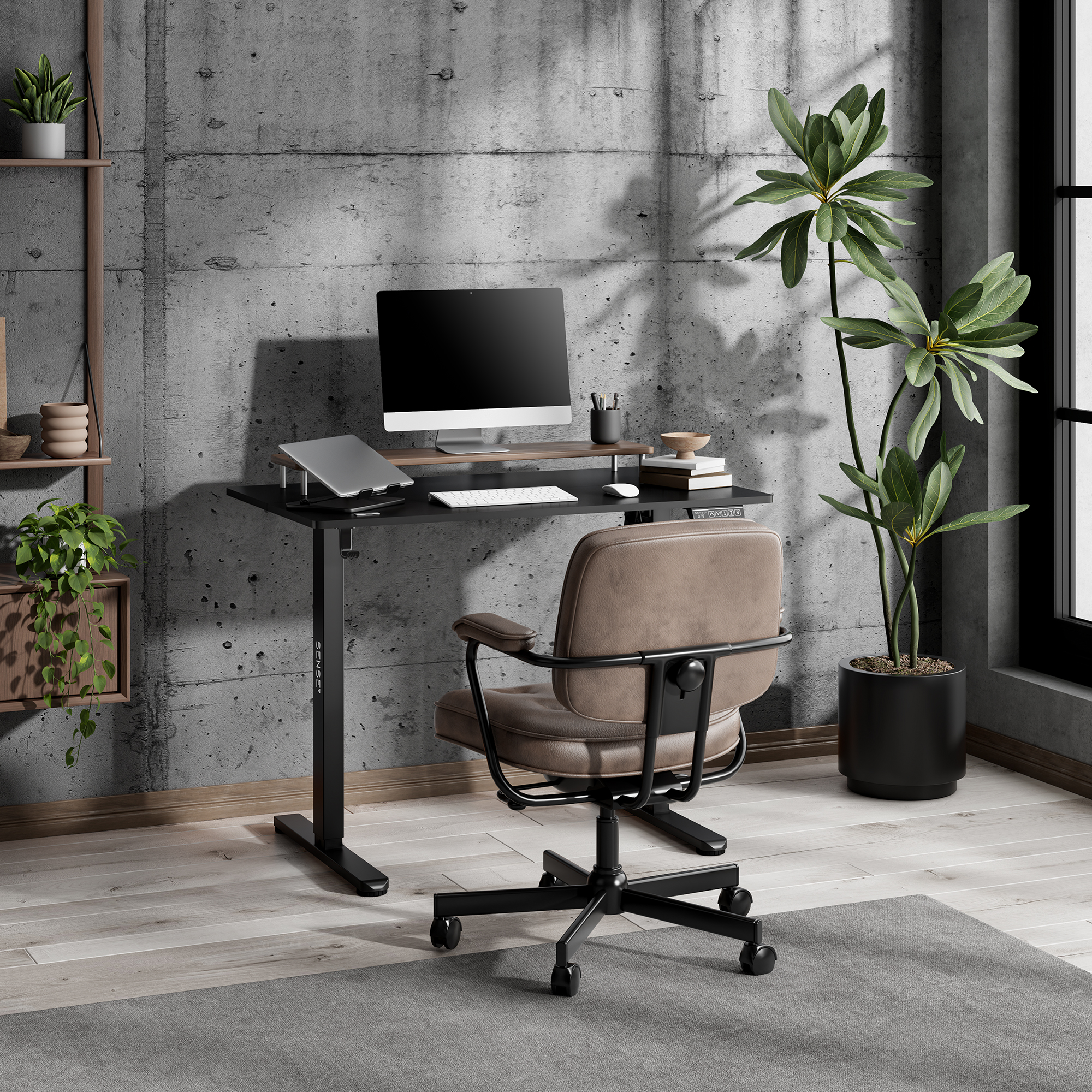 Una oficina moderna con escritorio negro ajustable, ordenador, silla marrón y plantas en maceta ante una pared de hormigón.