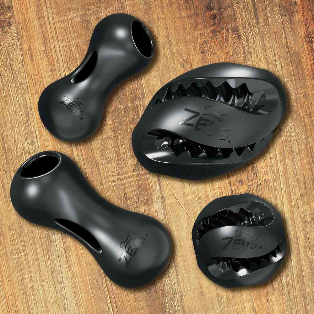 Cuatro juguetes de goma negra Zeus para perros con formas de hueso y pelota sobre suelo de madera.