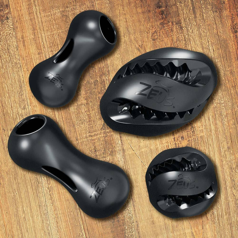 Cuatro juguetes negros para perros Zeus con aberturas y bordes dentados sobre un fondo de madera.
