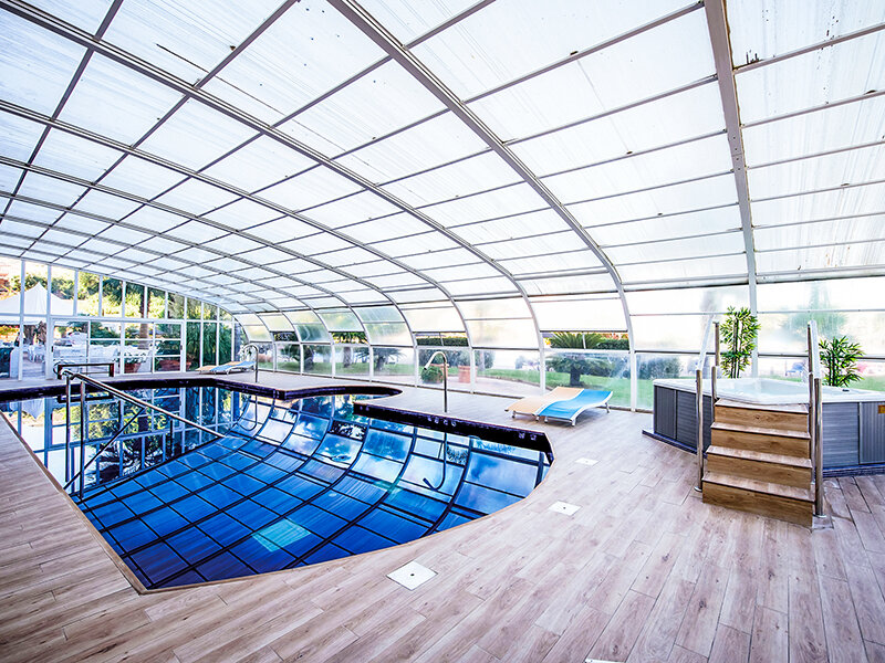 Piscina cubierta con jacuzzi, suelo de madera y grandes puertas de vidrio que conducen al exterior.
