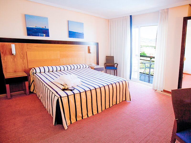 Una habitacion de hotel luminosa con una cama grande de rayas azules y blancas.