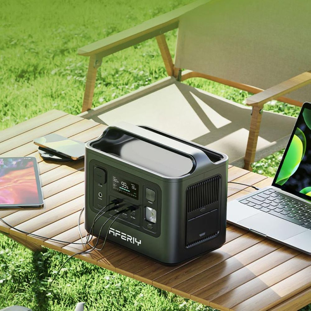Una estación de energía portátil en una mesa de madera al aire libre alimenta dispositivos como un portátil y una tablet.