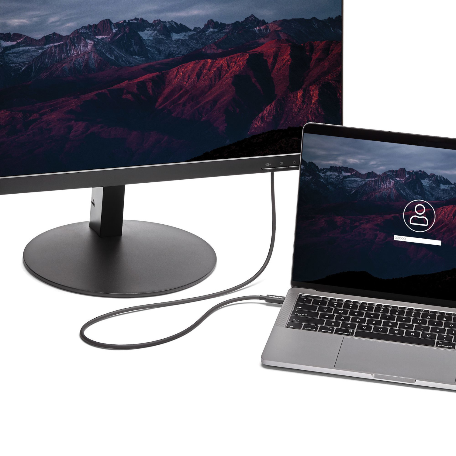 Un computer portatile è collegato a un grande monitor tramite un cavo, entrambi mostrano paesaggi montani.