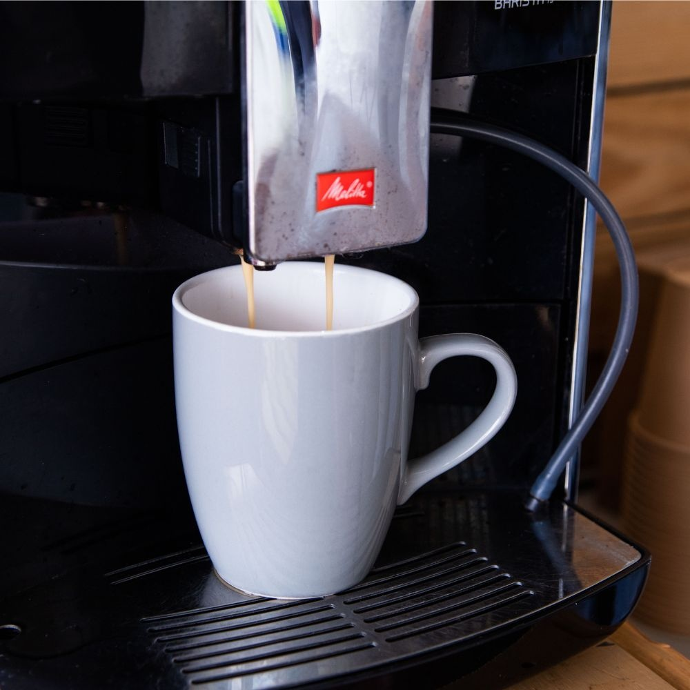 A coffee machine pours fresh coffee into a grey mug sitting on the drip tray.