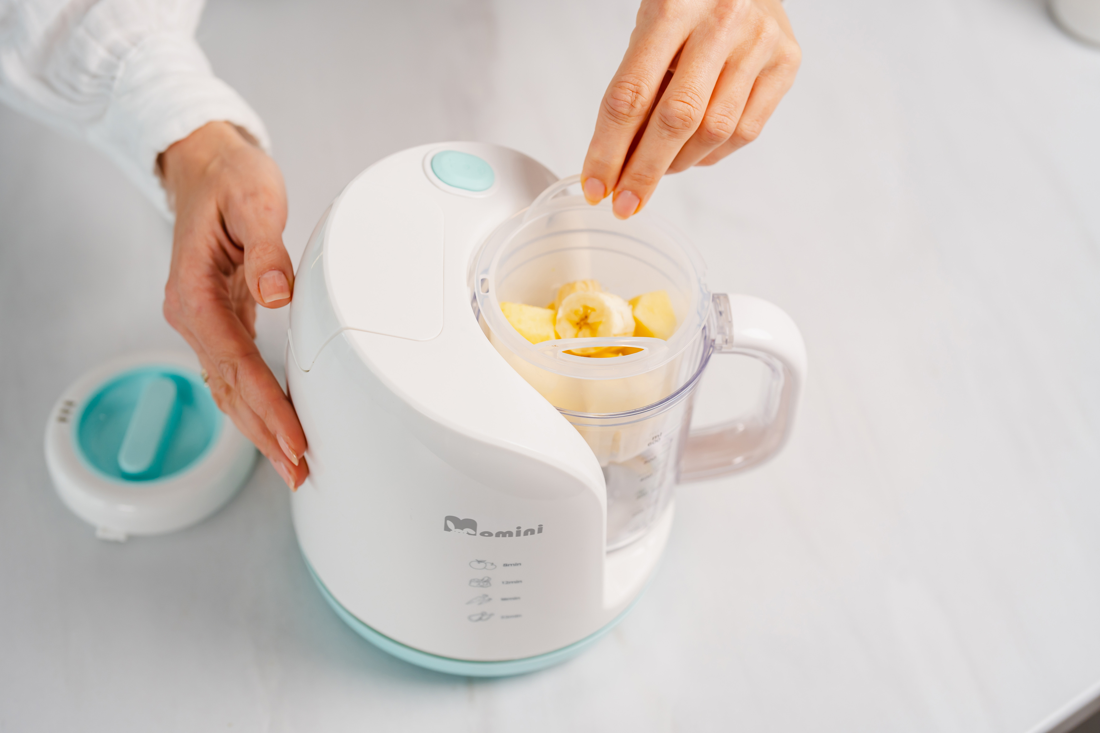 Osoba umieszcza pojemnik z kawałkami banana w białym mini blenderze.
