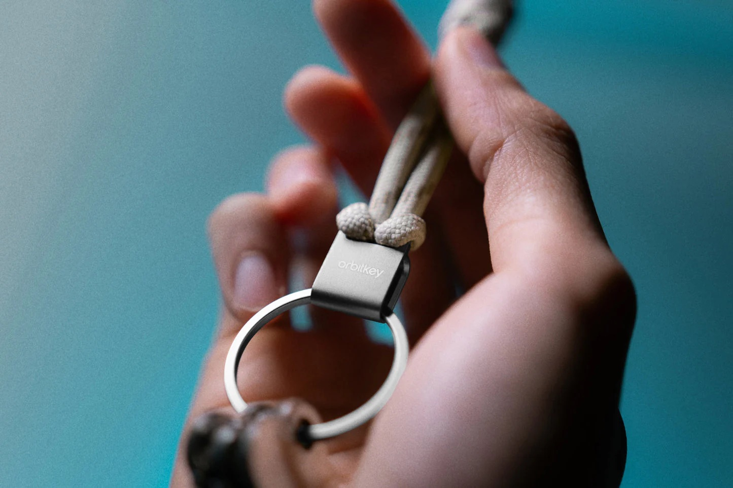 Osoba trzyma metalowy pierścień Orbitkey z beżowym paskiem na niebieskim tle.