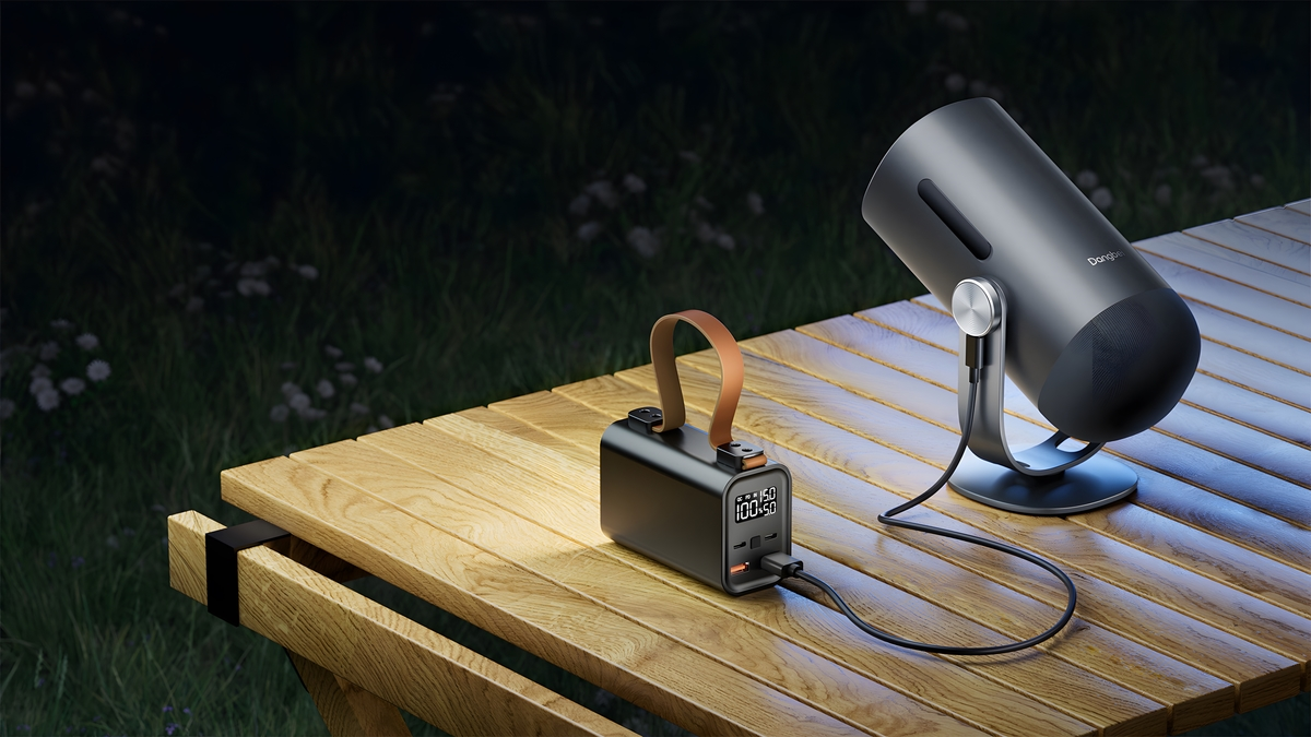 Een powerbank voedt 's avonds een cilindrische projector op een houten tafel.