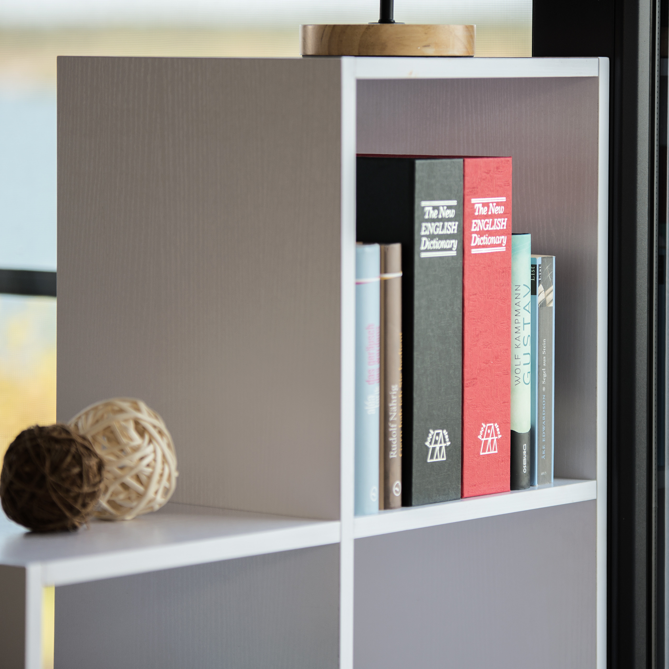 Ein weißes Würfelregal enthält englische Wörterbücher, Bücher und dekorative geflochtene Kugeln.