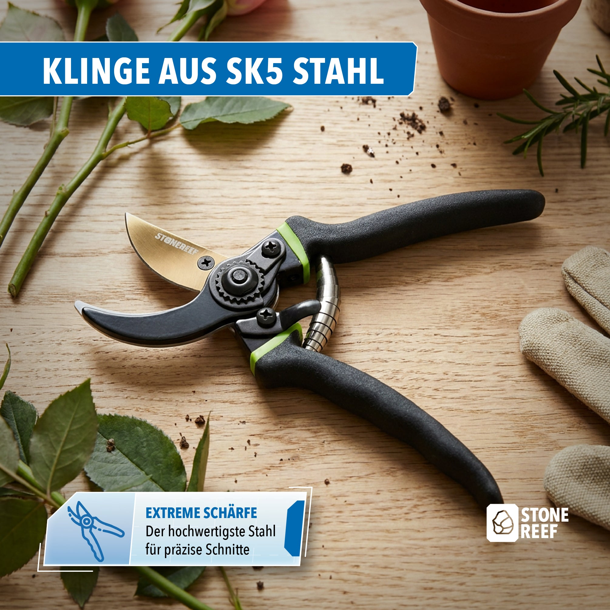 Garten-Astschere mit schwarzem Griff auf Holztisch, umgeben von Rosenstängeln, einem Pflanzentopf und Gartenhandschuhen.