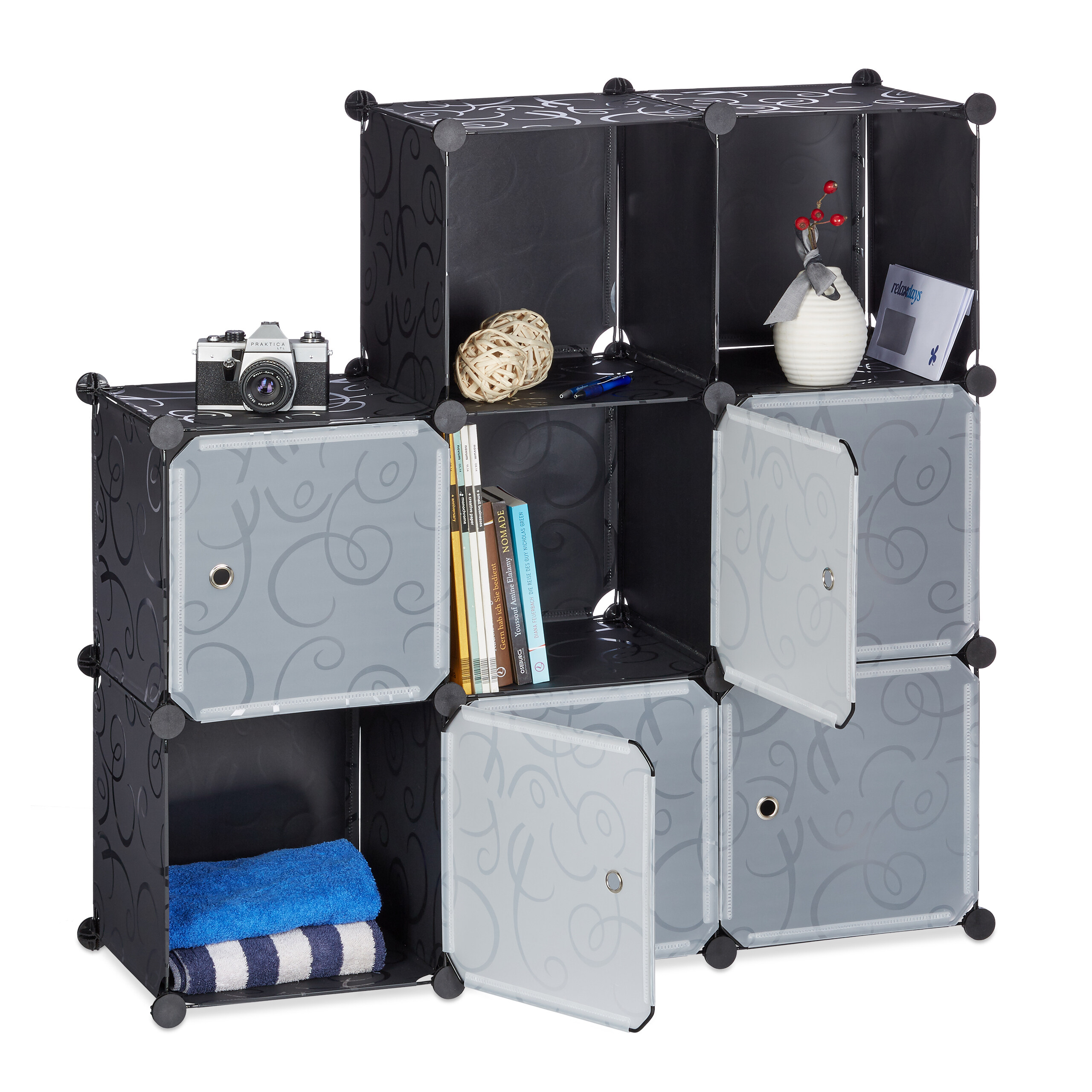 Ein modulares schwarz-graues Regal hält Bücher, Handtücher, eine Vase und eine Kamera vor weißem Hintergrund.