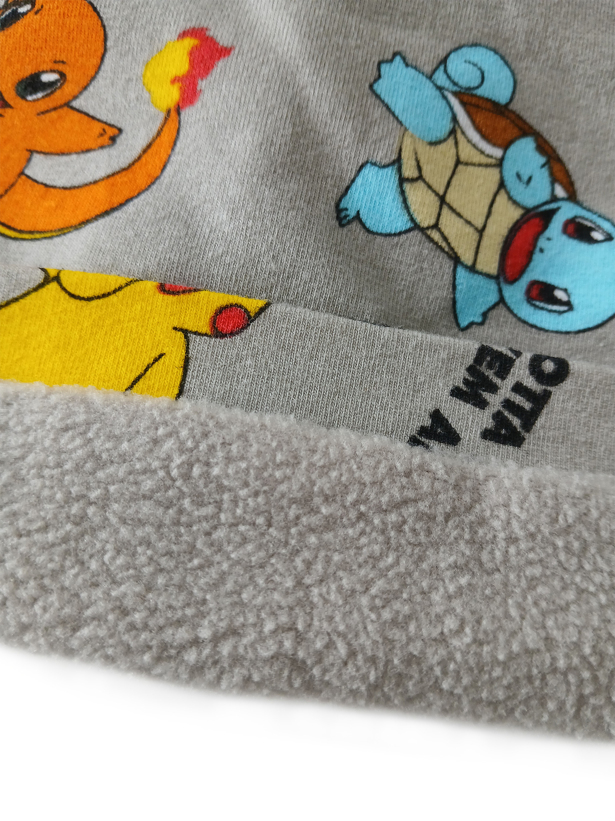 Grauer Stoff mit Pokémon-Motiven wie Charmander, Squirtle und Pikachu sowie einem flauschigen Saum.