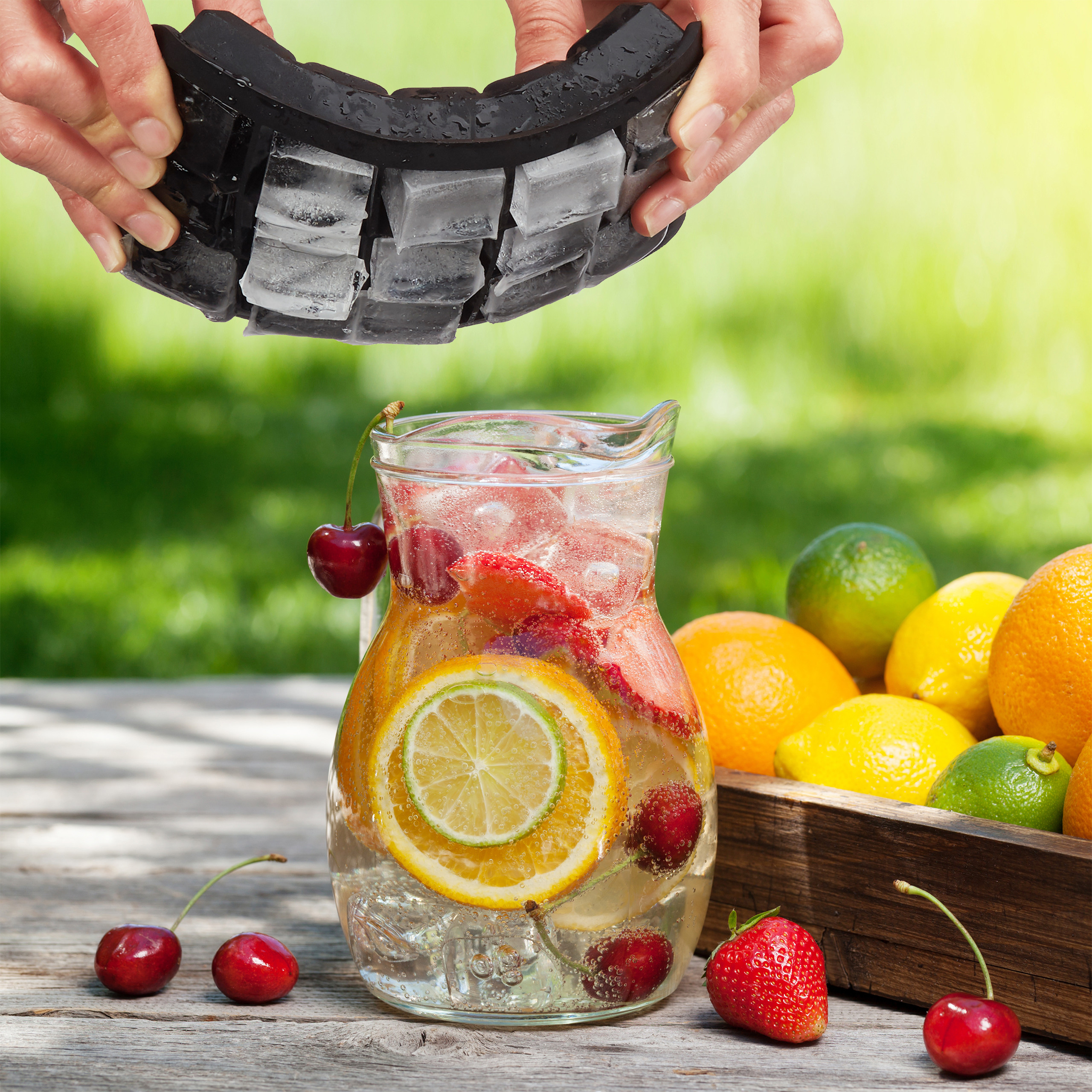 Hände entleeren eine Eisschale über einer Fruchtlimonade in einem Glas, neben frischem Obst.