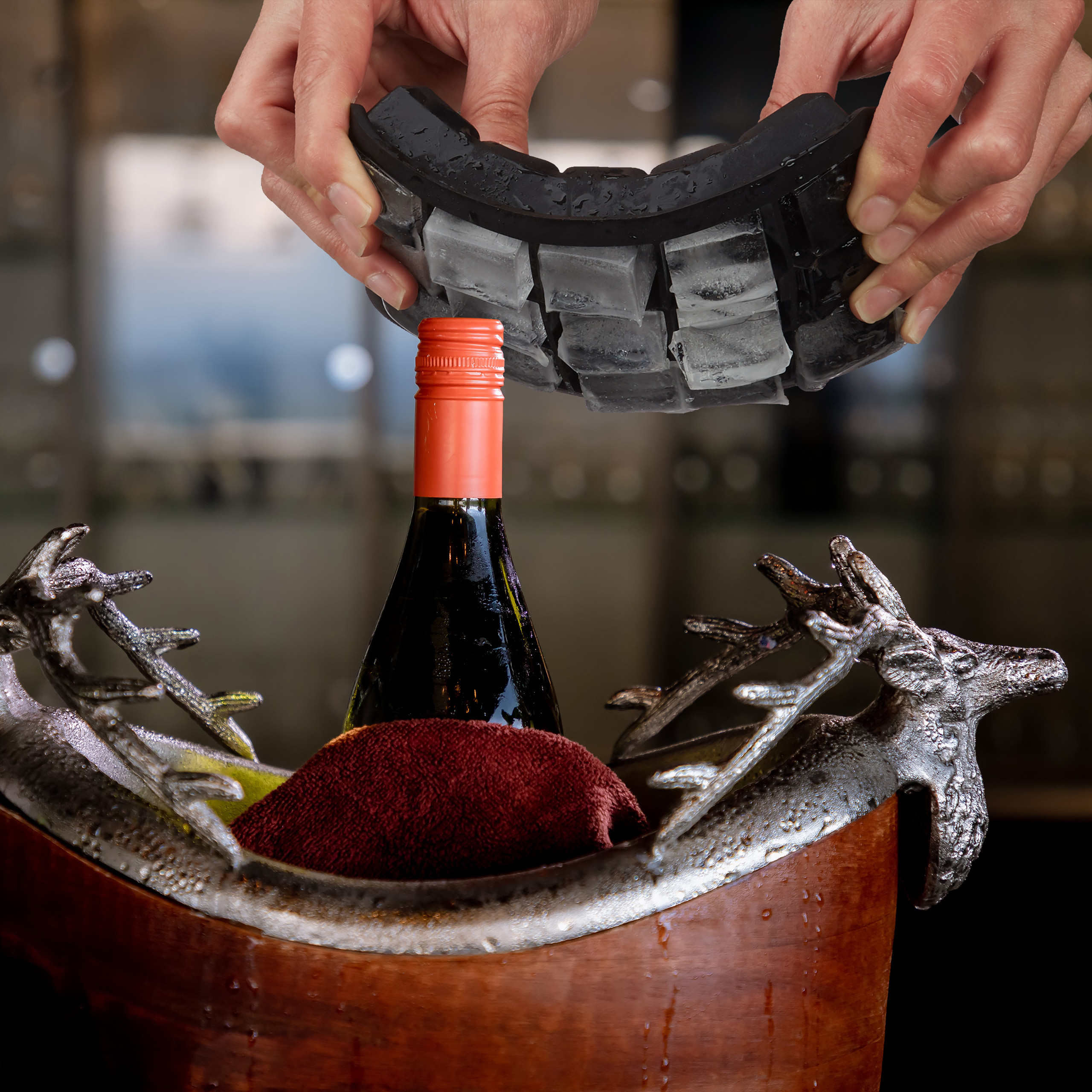 Hände biegen eine schwarze Silikon-Eiswürfelform über eine Weinflasche in einem verzierten Eiskübel.