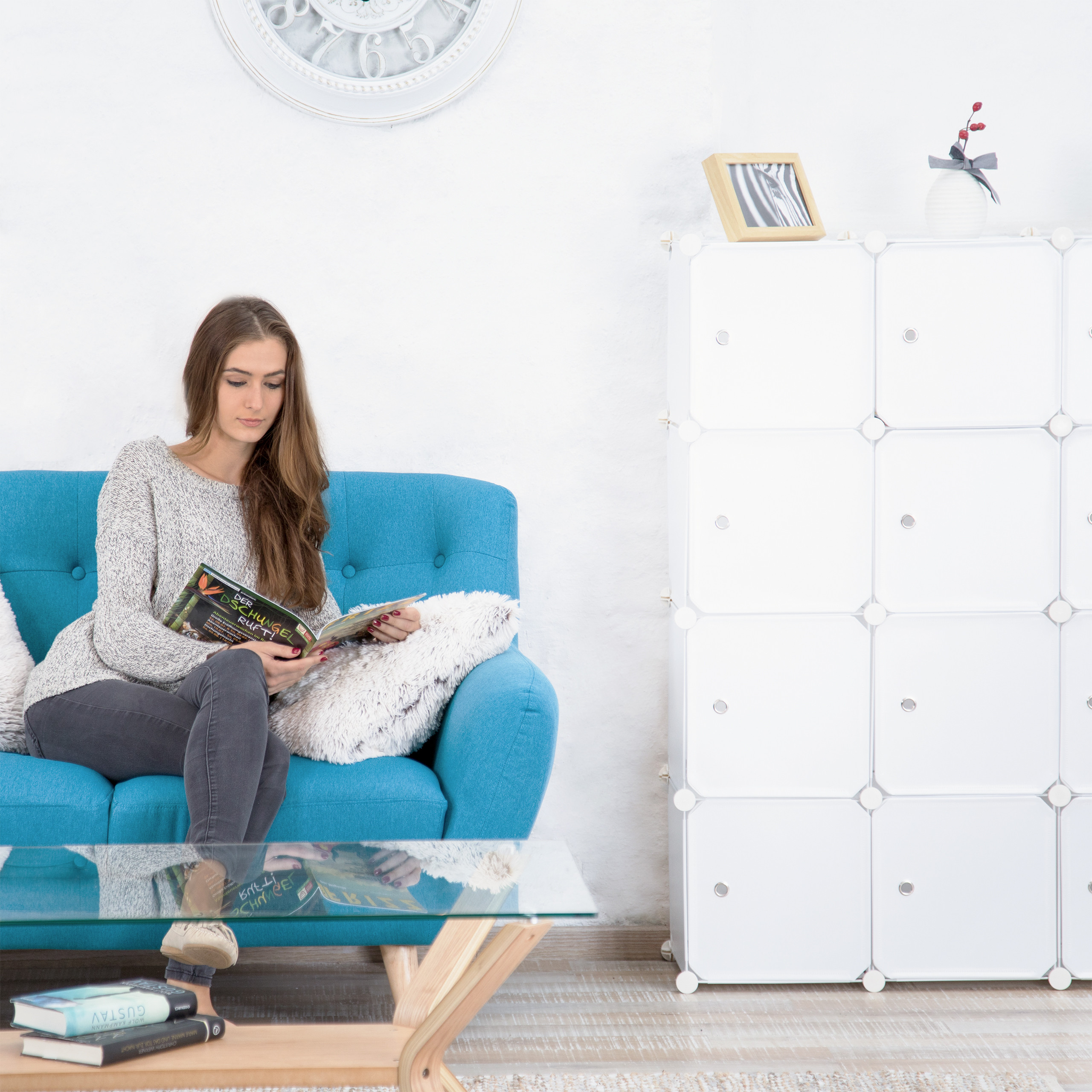 Eine Frau sitzt auf einem blauen Sofa und liest ein Magazin in einem hellen Zimmer.