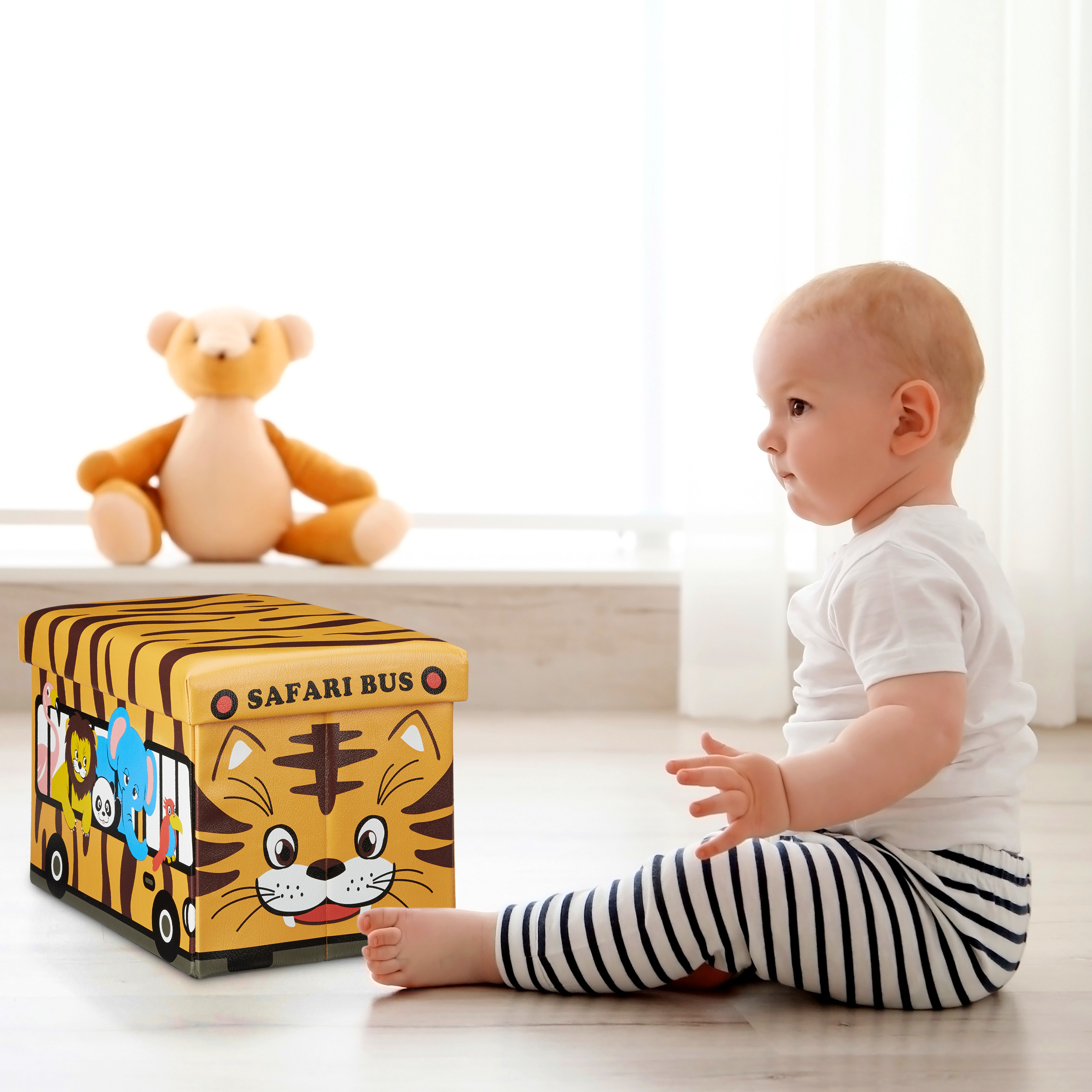 Ein Baby sitzt auf dem Boden nahe einer Spielzeugkiste im Tiger-Design, dahinter ein Teddybär.