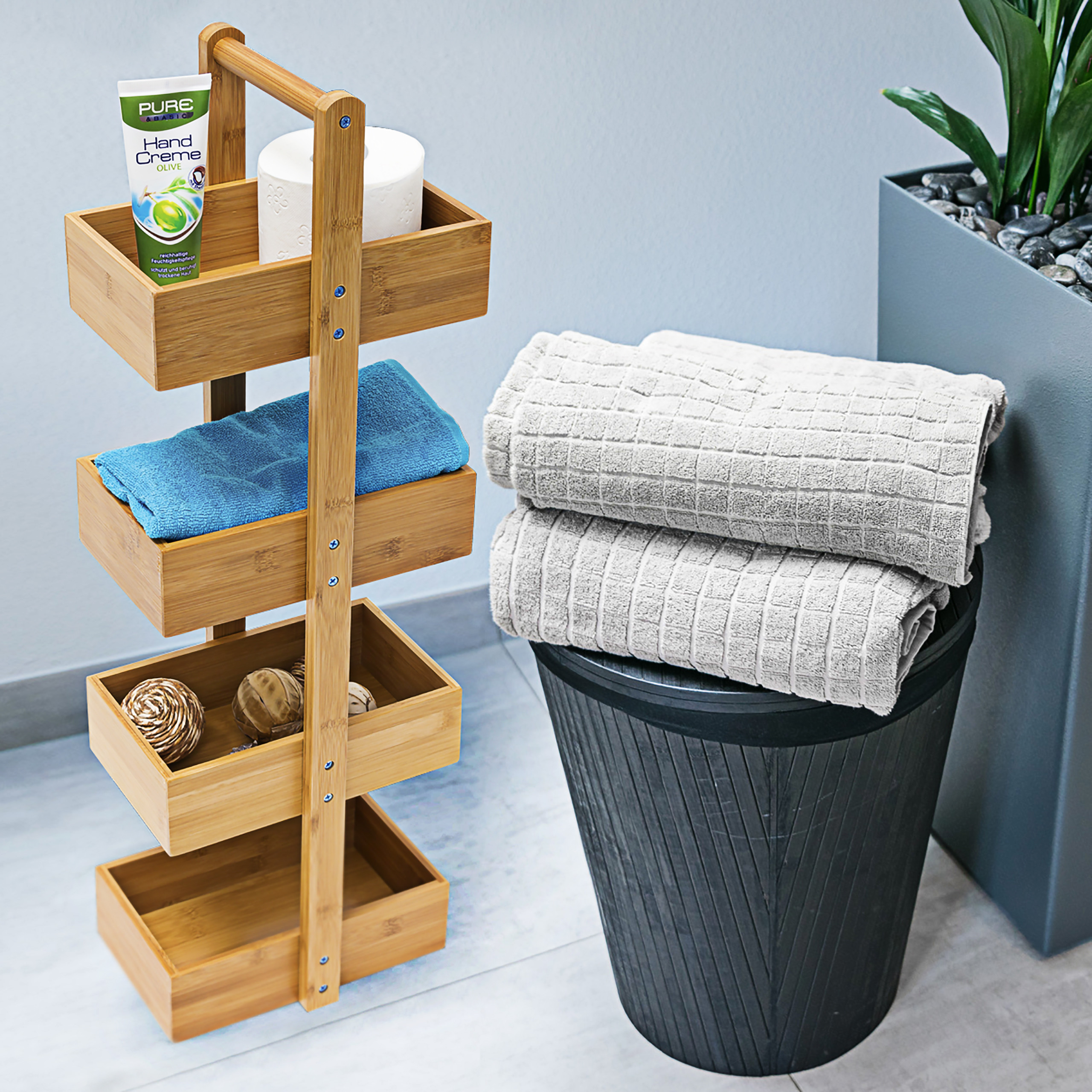 Ein Holzregal mit Handcreme und Handtüchern, ein schwarzer Wäschekorb mit Handtüchern und eine Topfpflanze.