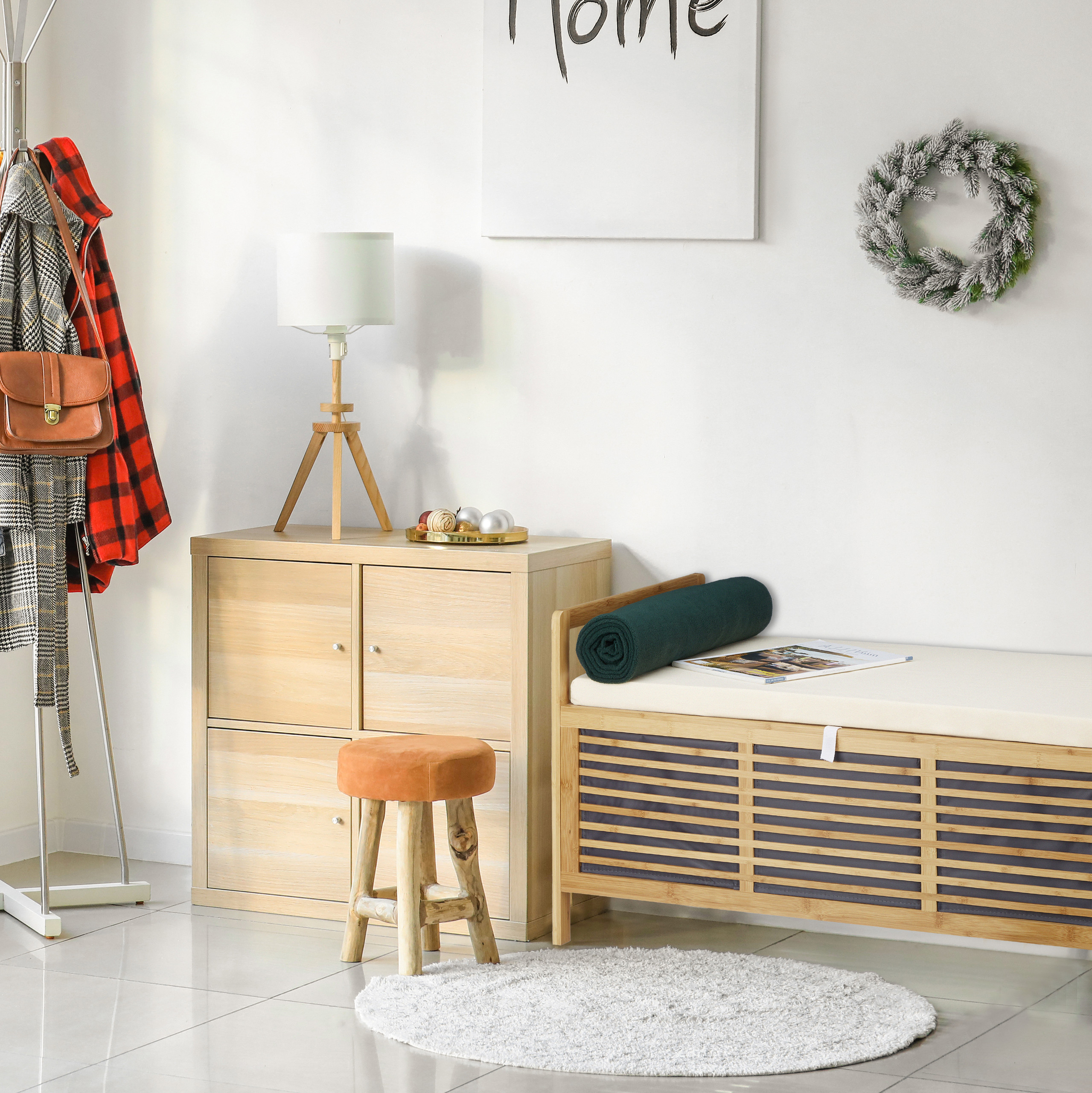 Gemütlicher Raum mit Holzschrank, Lampe, Bank mit gerollter Decke, kleinem Hocker und einem Kranz an der Wand.