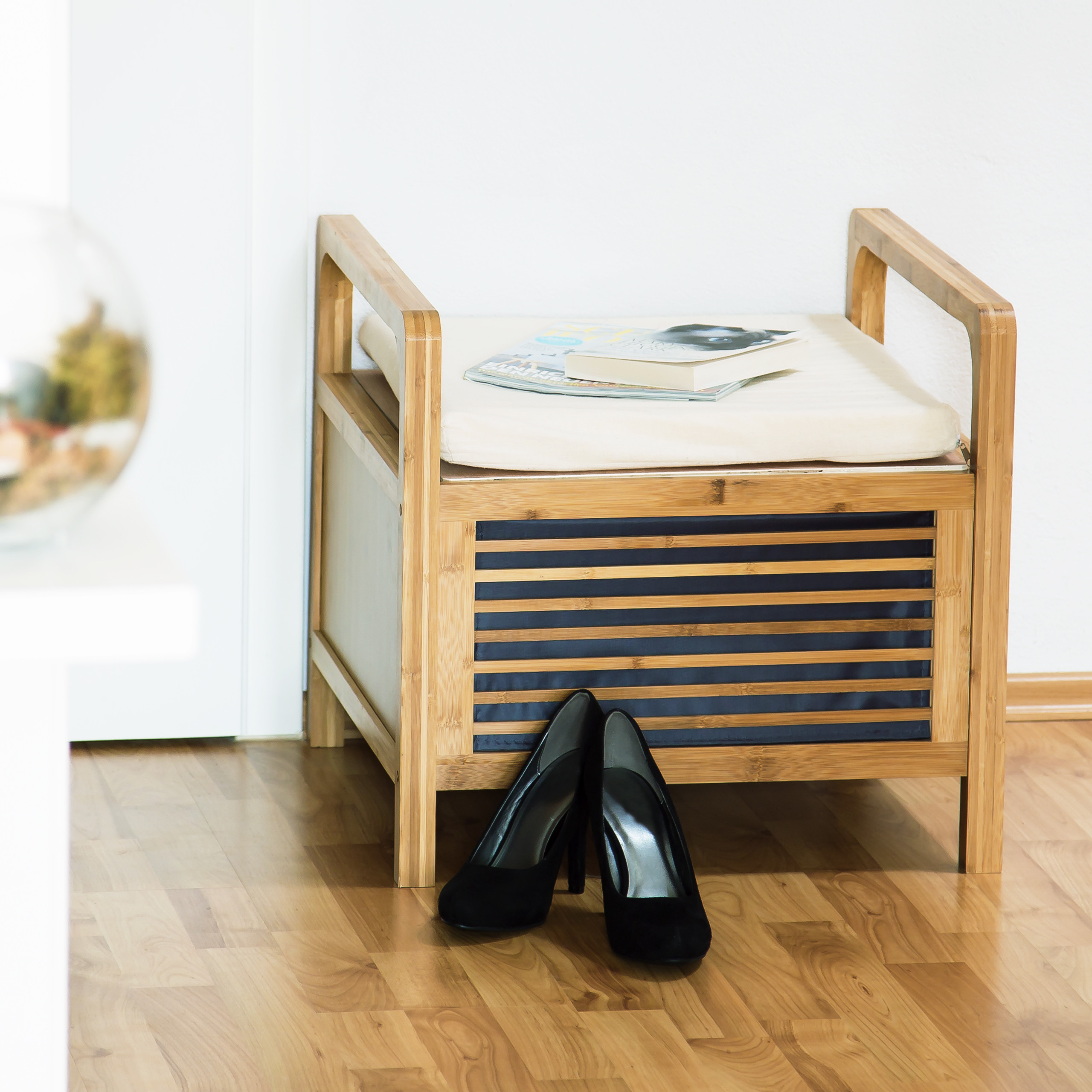 Eine Holzsitzbank mit Kissen, darauf liegen Magazine; davor stehen schwarze High Heels auf Parkett.