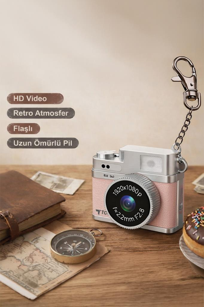Ahşap masa üzerinde kitap, pusula ve donut ile birlikte duran pembe ve gümüş renkli mini retro kamera.