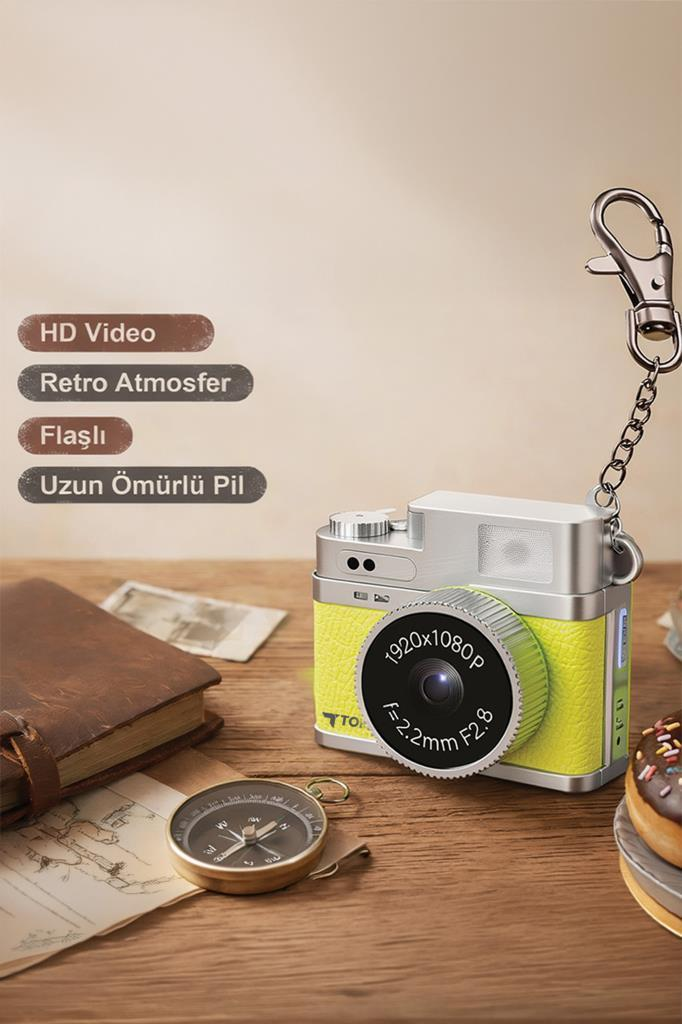 Anahtarlıklı küçük, sarı ve gümüş renkli retro kamera, kitaplar ve bir pusula ile çevrili ahşap masa üzerinde duruyor.