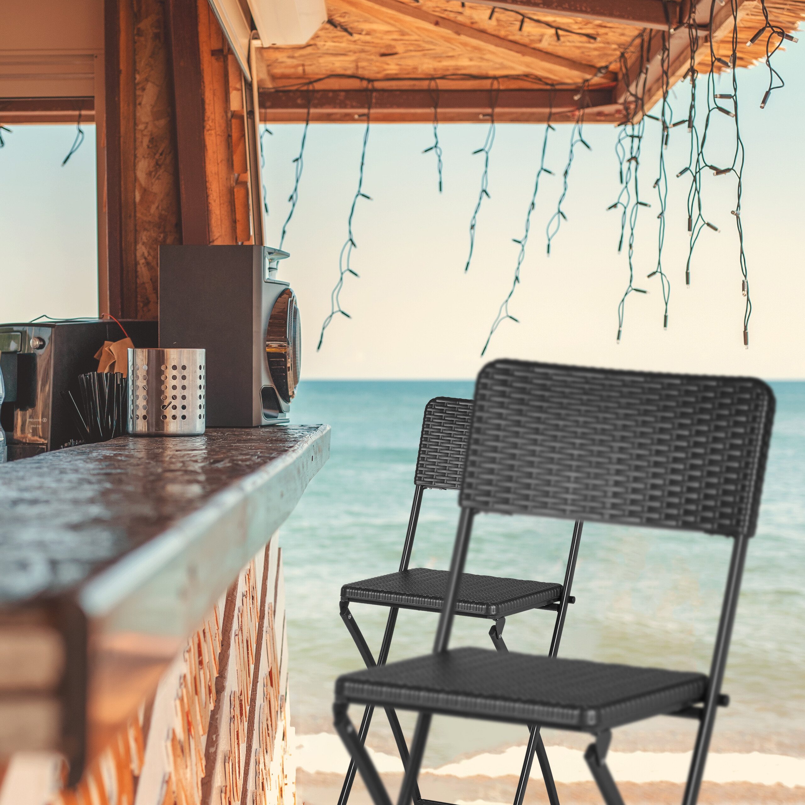 Eine Strandbar mit dunklen Stühlen, einer Musikanlage und Blick auf das blaue Meer.