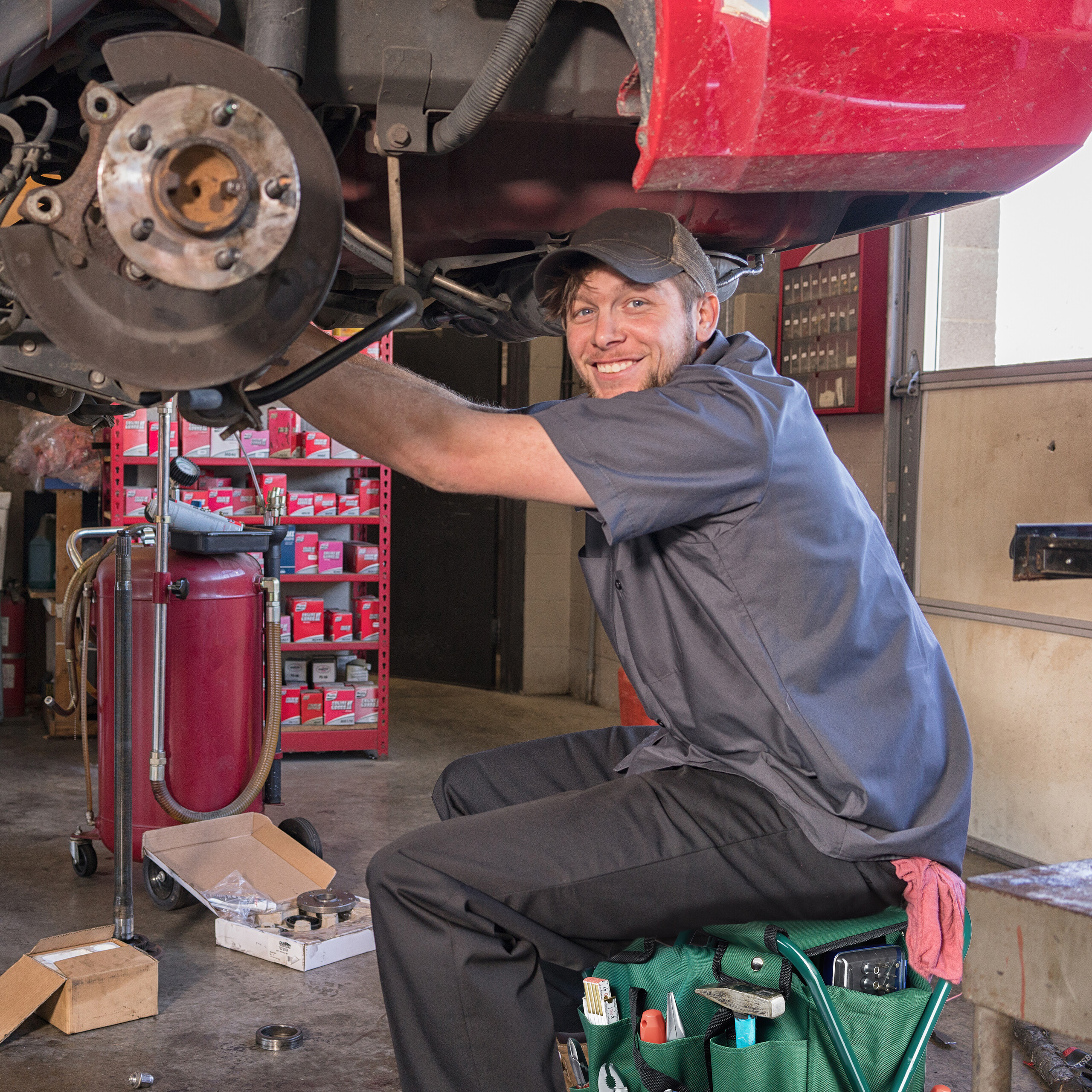 Ein lächelnder Mechaniker arbeitet in einer Werkstatt am Bremssystem eines roten Autos.