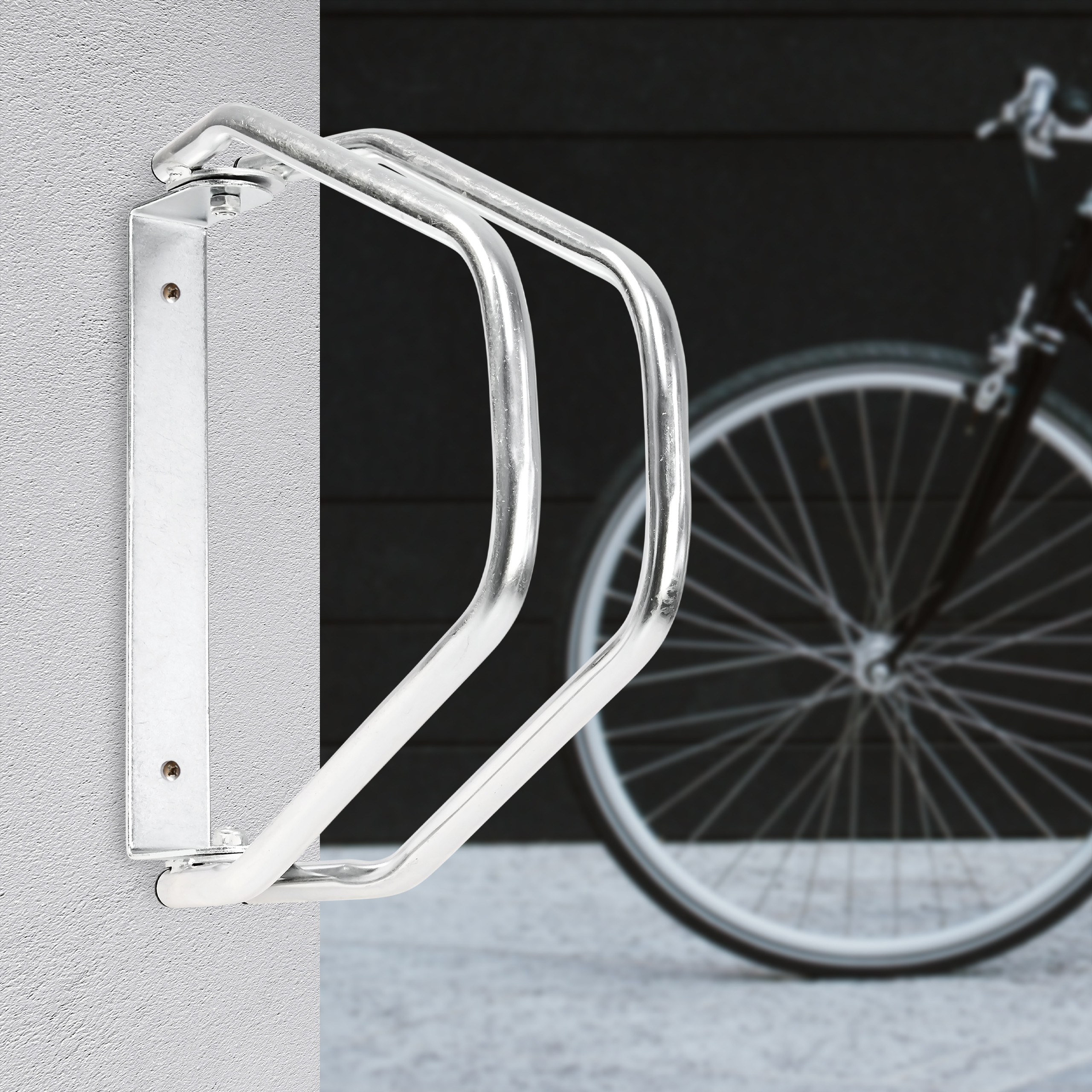 Ein silberner Metall-Fahrradständer ist an einer Wand befestigt, im Hintergrund steht ein Fahrrad.