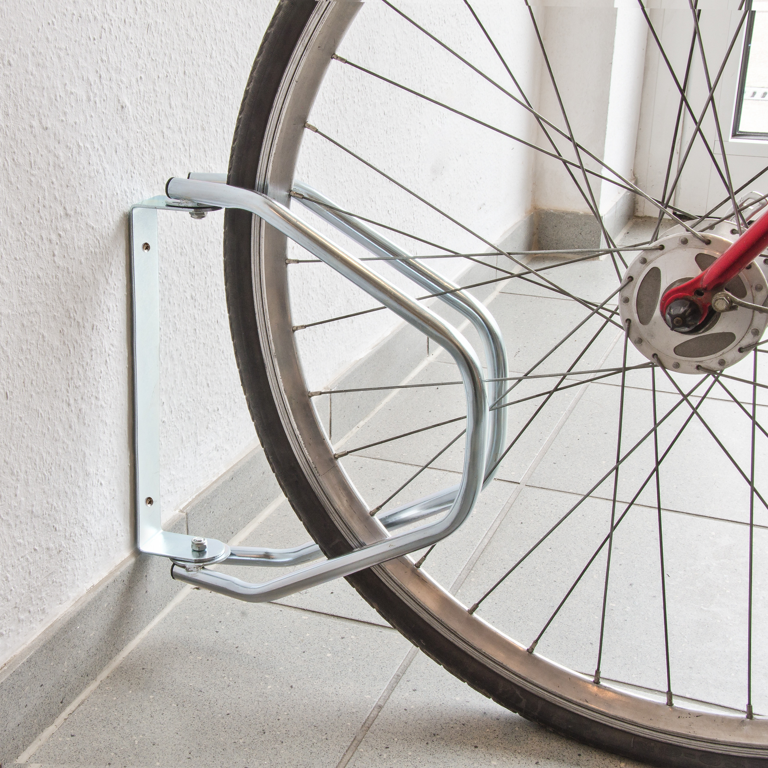 Ein Fahrradvorderreifen ruht in einem Metall-Wandhalter auf grauem Fliesenboden.