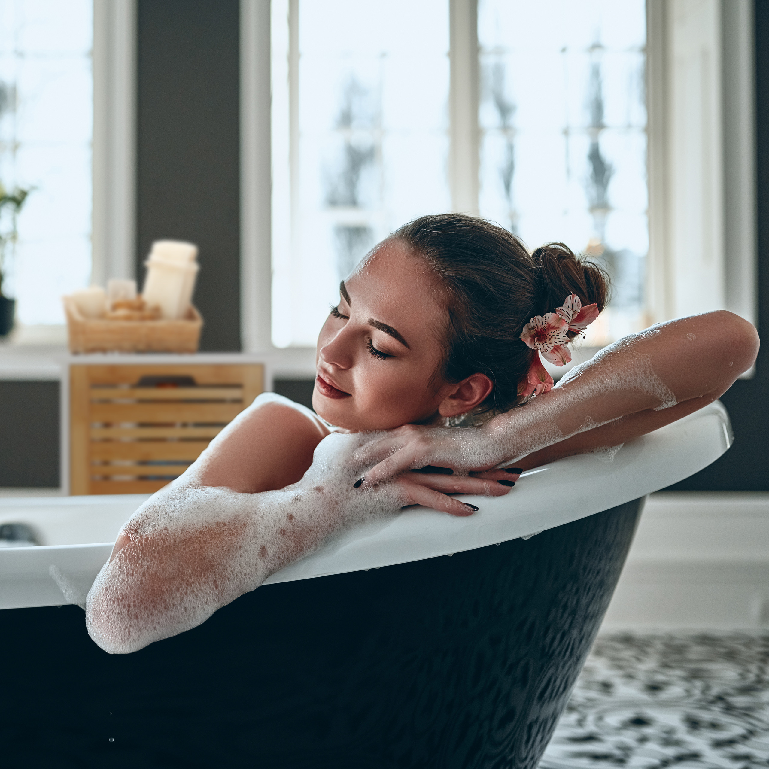 Eine Frau mit einer Blume im Haar entspannt in einer Badewanne mit Schaum.