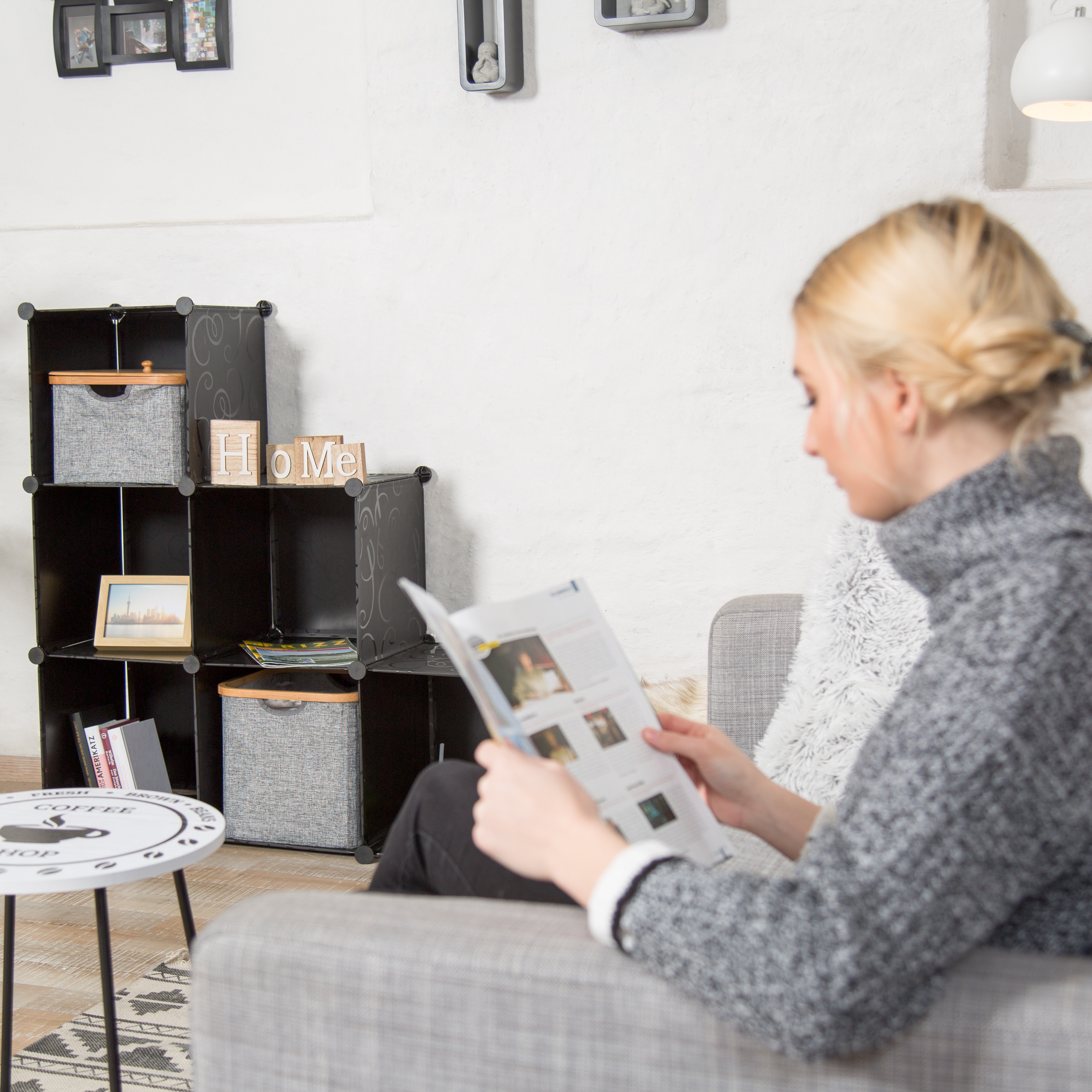 Eine blonde Frau in einem grauen Rollkragenpullover sitzt auf einem Sofa und liest ein Magazin.