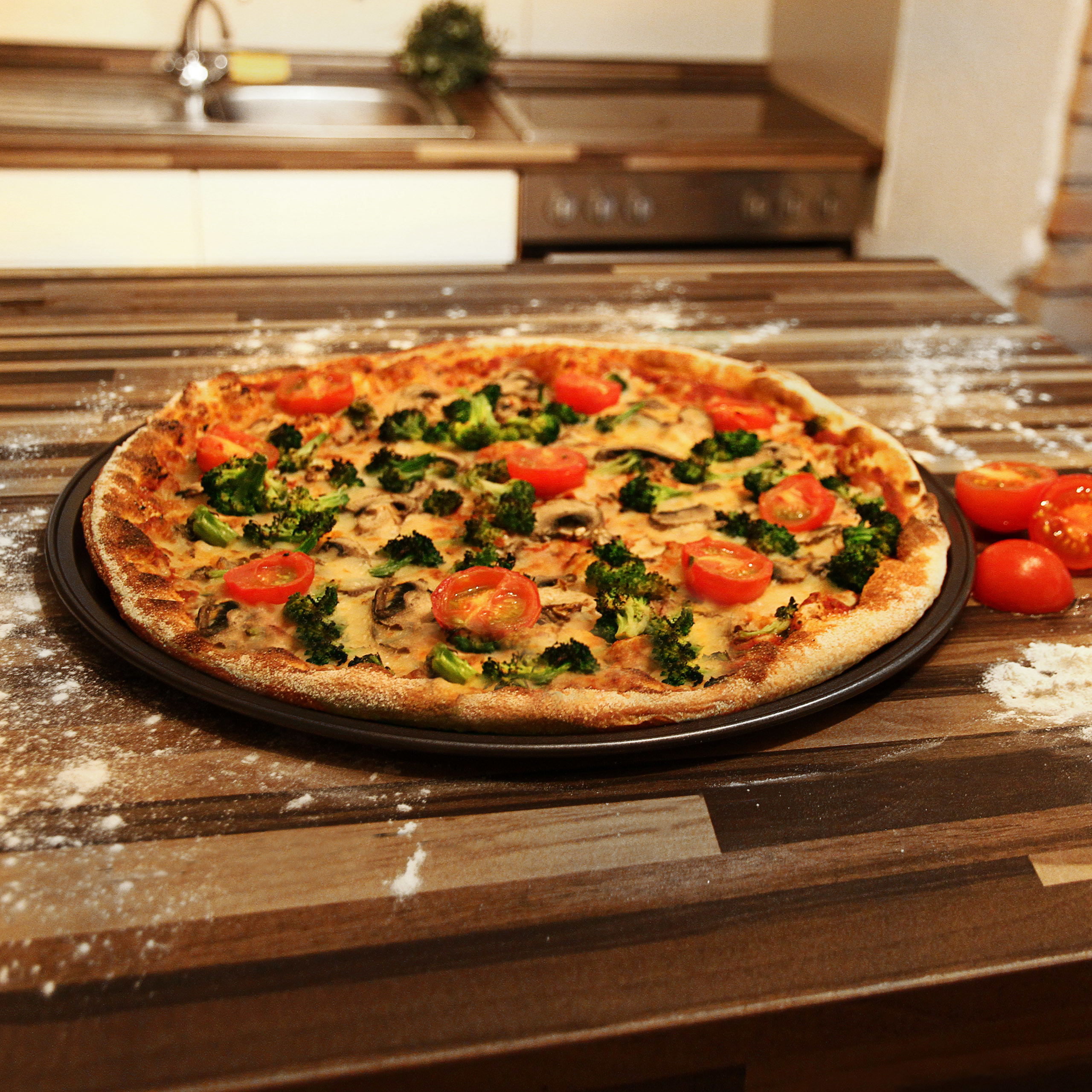 Pizza mit Brokkoli, Tomaten und Pilzen auf Holztisch in Küche.