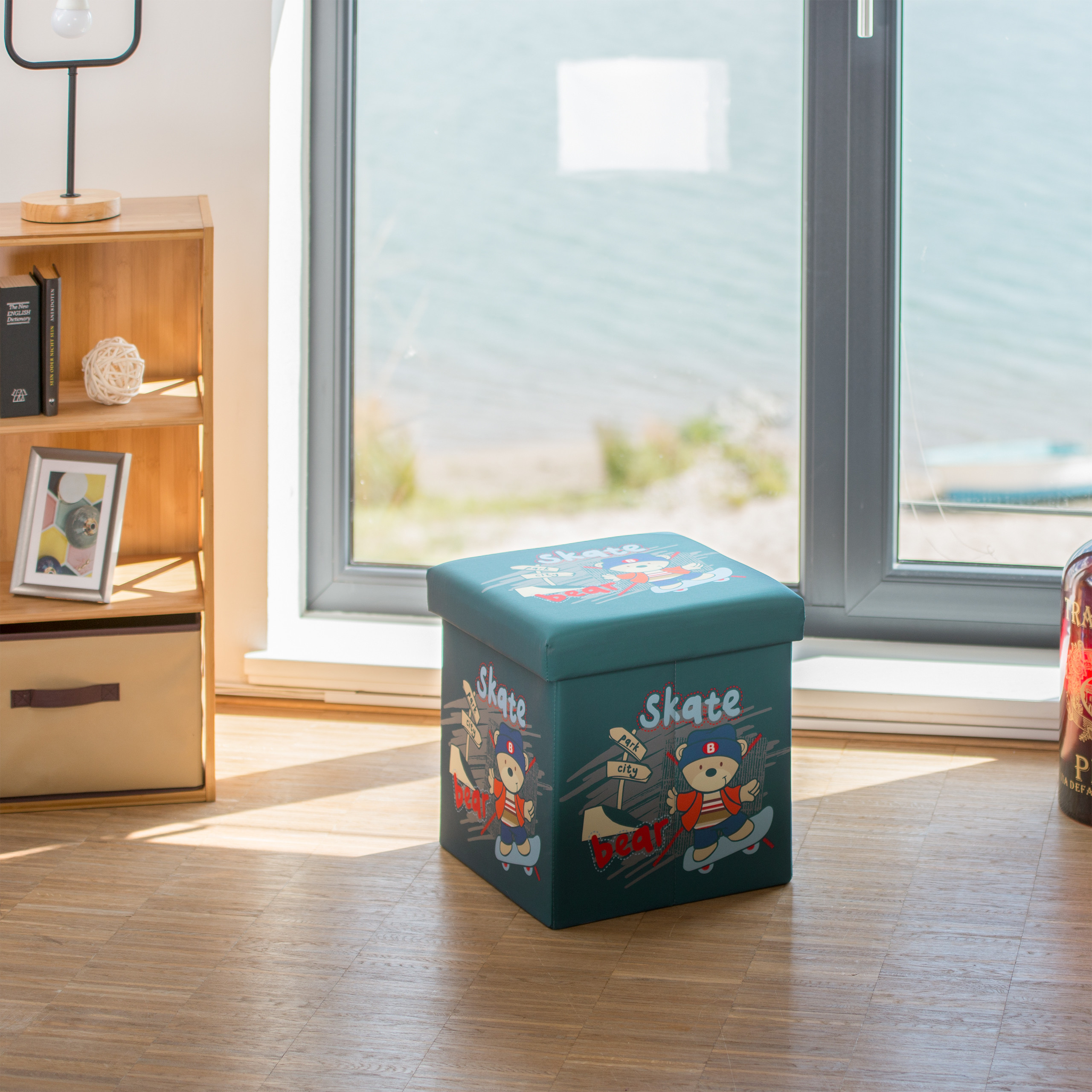 Ein blauer Spielzeughocker mit Skate-Bär-Motiv steht auf Holzfußboden vor einem Fenster.