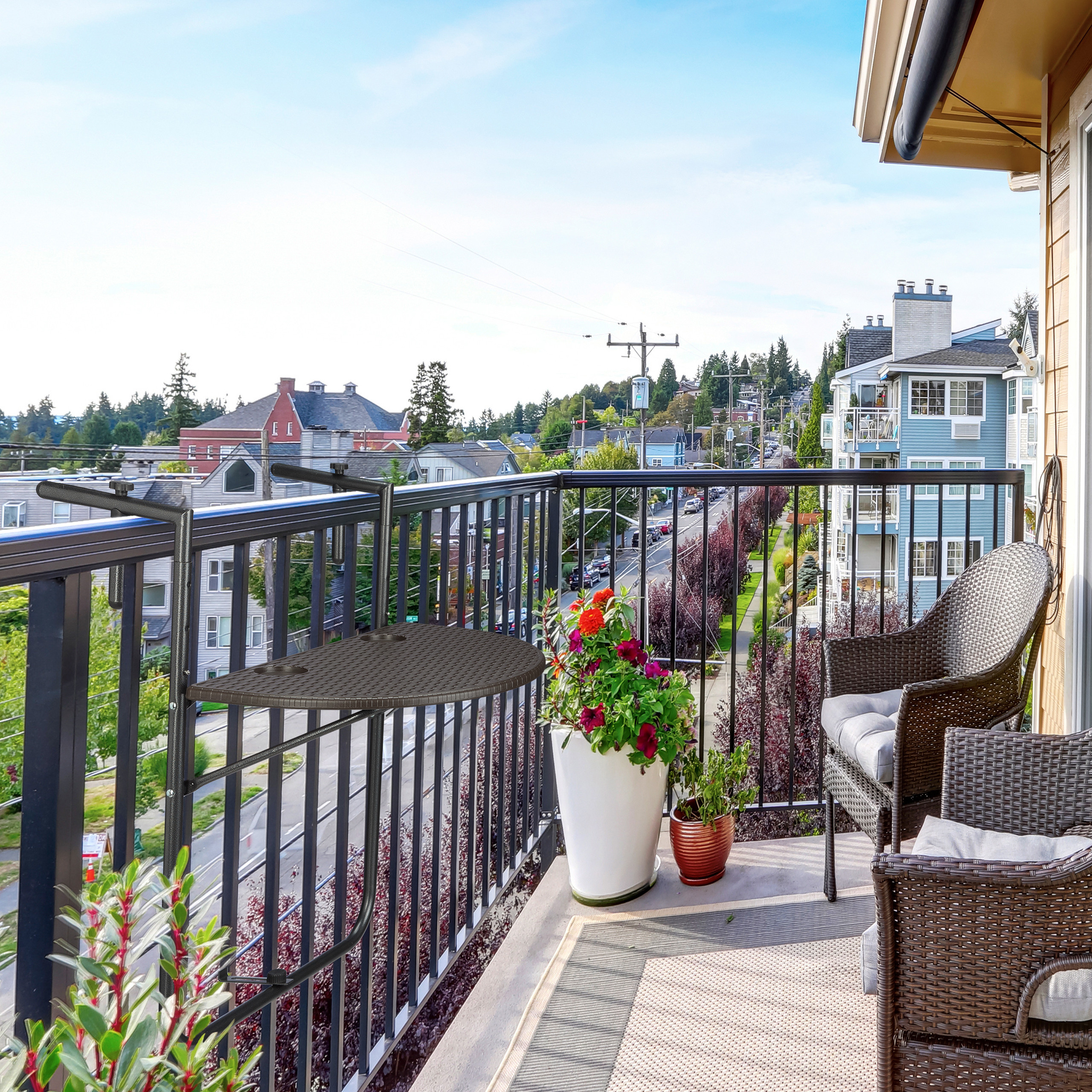 Balkon mit Rattanmöbeln, Hängetisch am Geländer, Pflanzenkübeln und Blick auf umliegende Häuser.