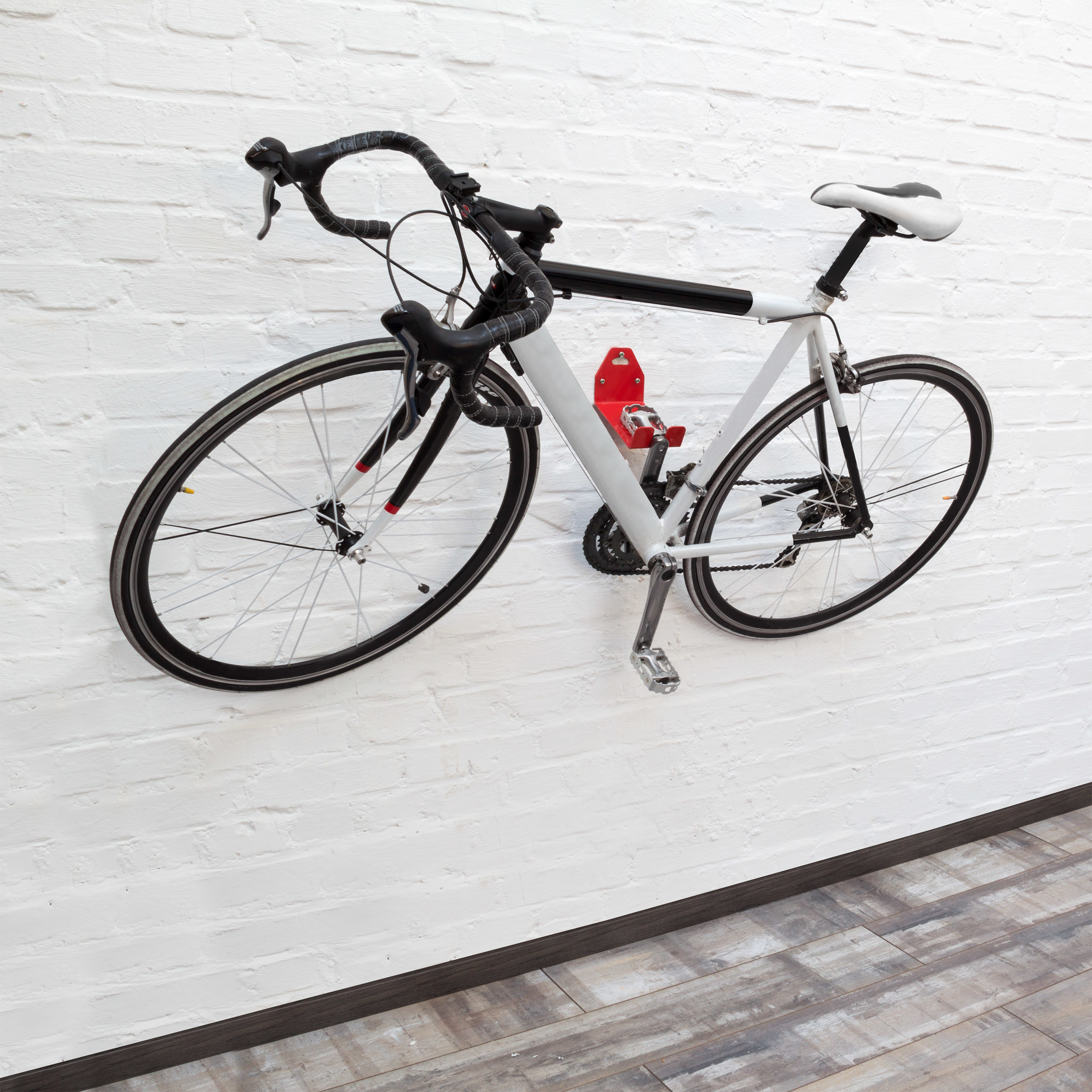 Ein weißes Rennrad hängt an einer Halterung an einer weißen Backsteinwand über einem grauen Holzboden.