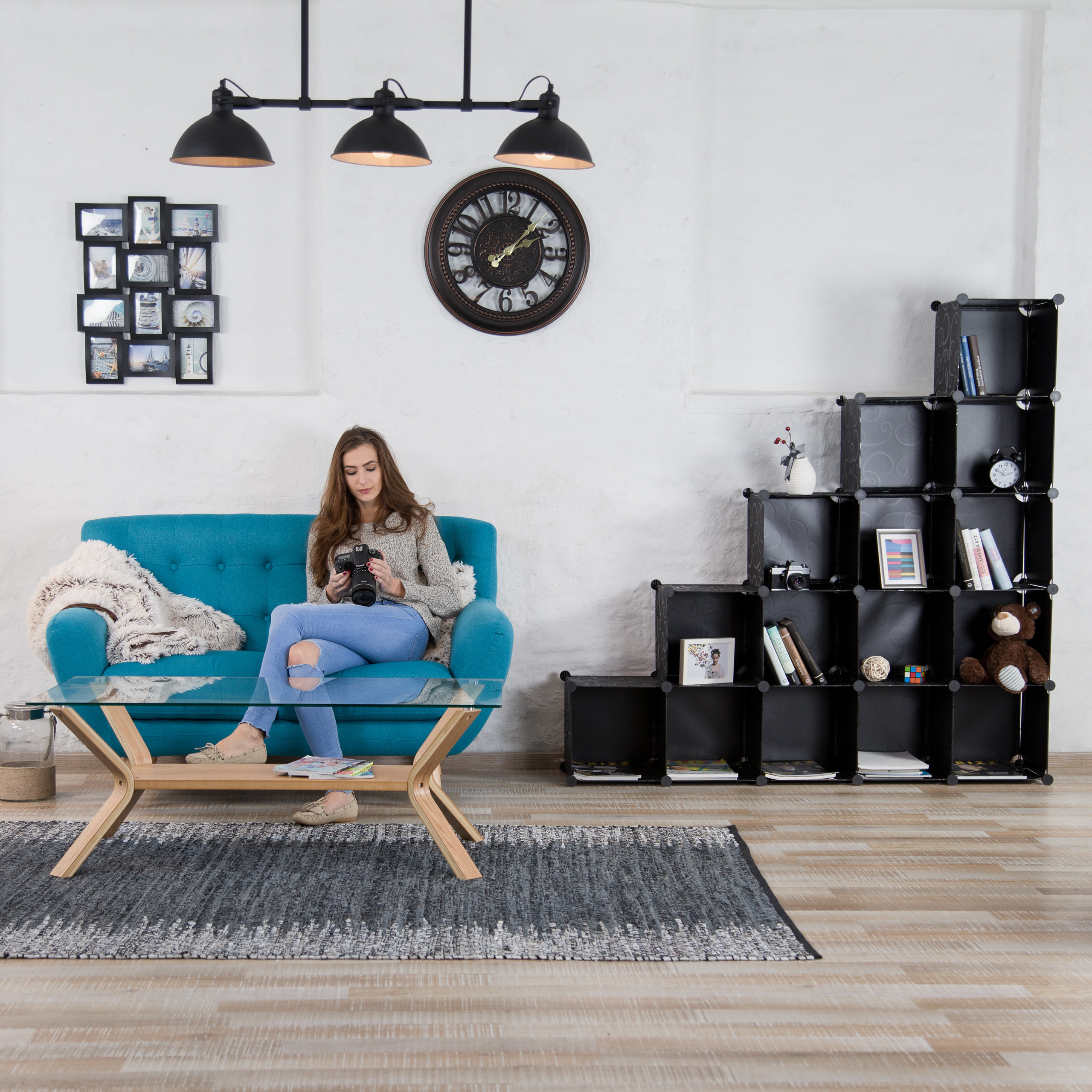 Eine Frau sitzt auf einem blauen Sofa und hält eine Kamera, vor einem Holztisch in einem hellen Zimmer.