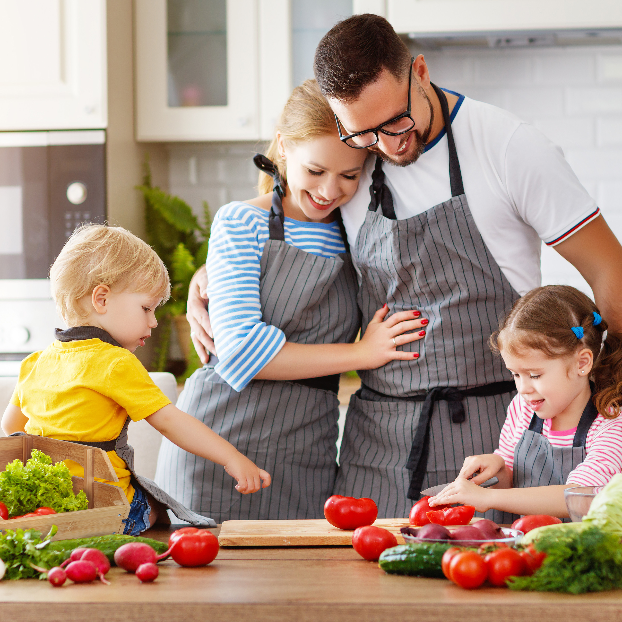 Eine Familie mit zwei Kindern kocht gemeinsam in einer hellen Küche und bereitet frisches Gemüse zu.