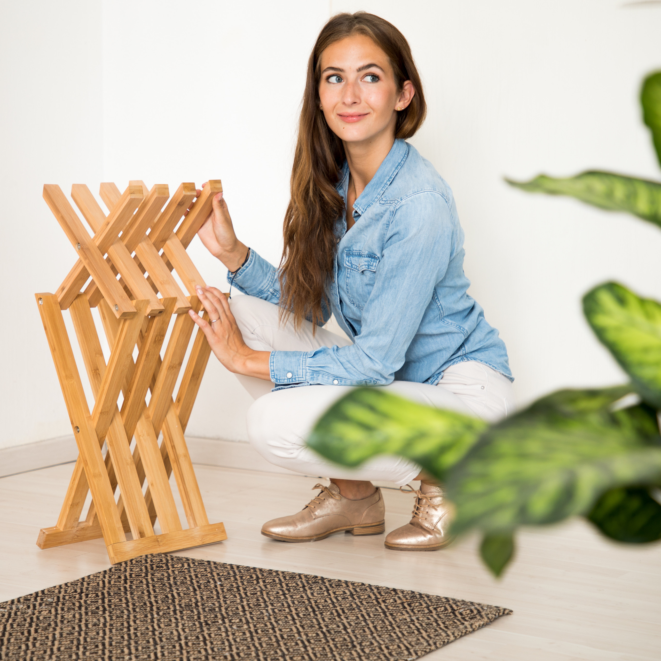 Eine Frau in Jeanshemd kniet neben einem Holzklappständer auf einem Teppich.
